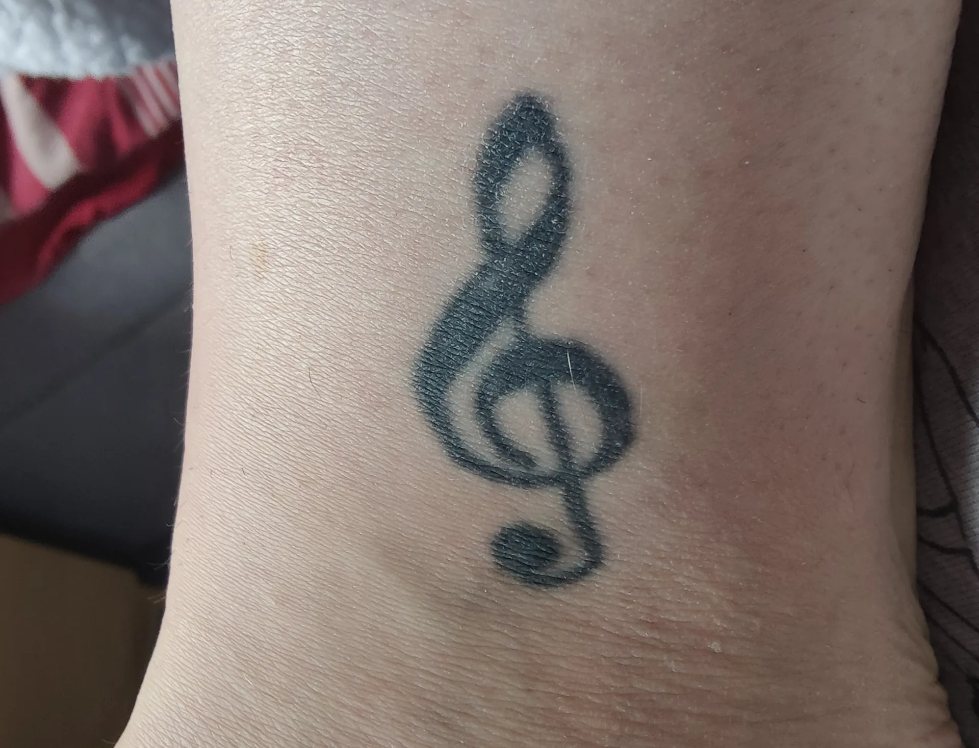 A tattoo of a treble clef adorns the skin.