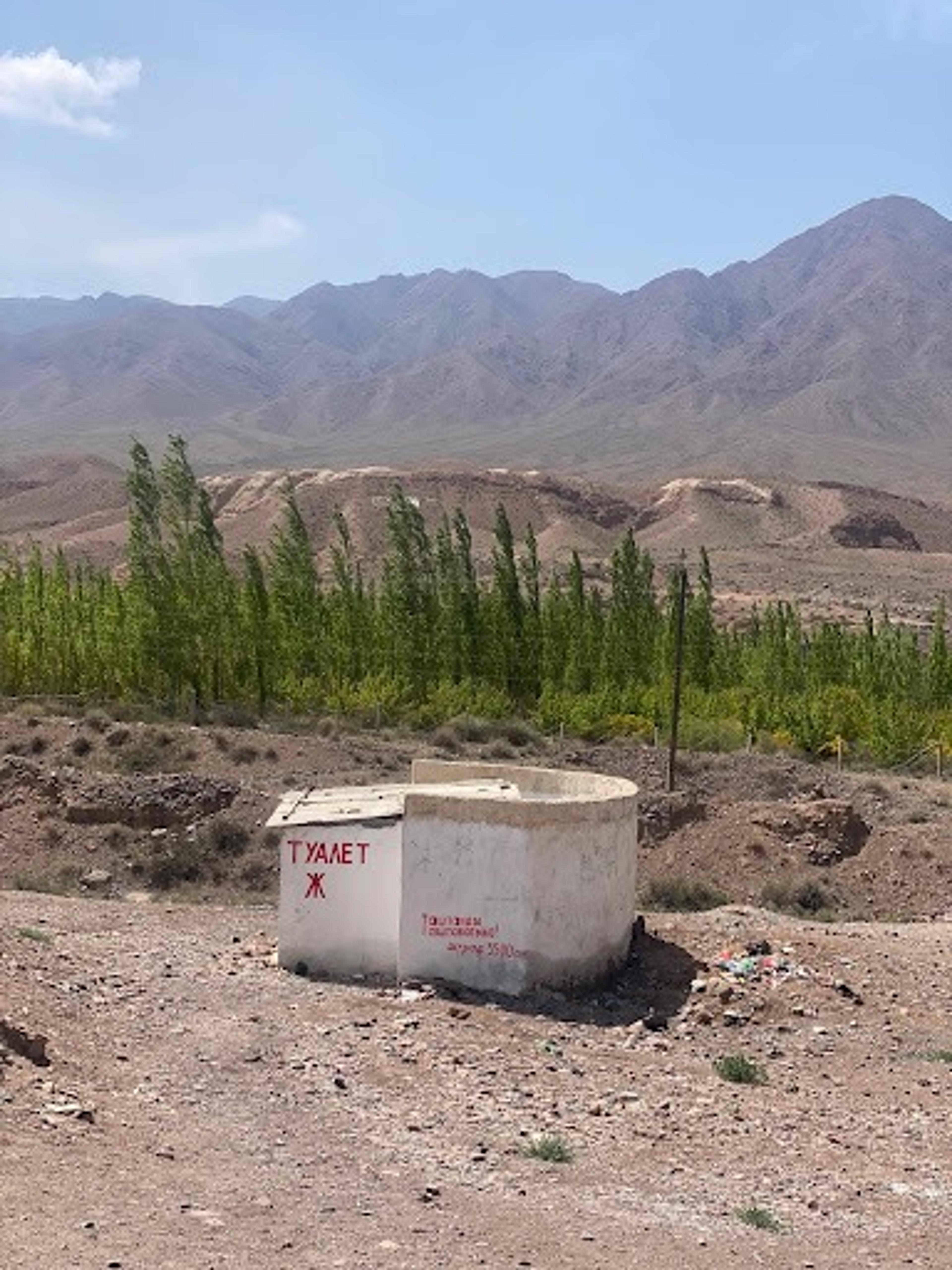 A simple concrete structure labeled toilet stands in a barren landscape near the Tian Shan mountains in Kyrgyzstan.