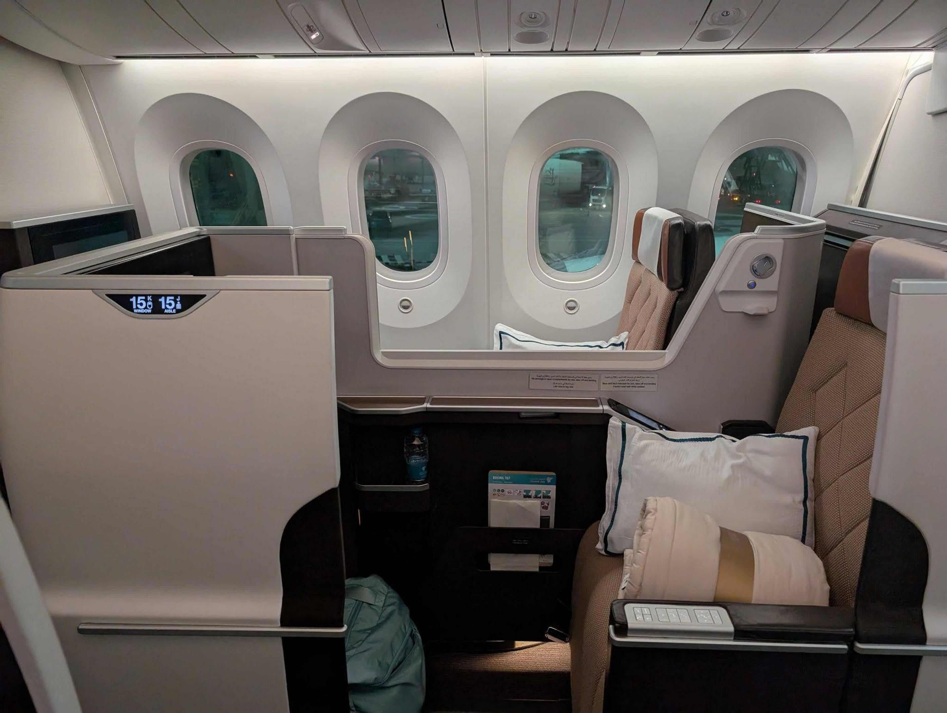 A luxurious business class seat aboard an aircraft, likely a Boeing 787 Dreamliner, features plush bedding and a sleek design for an enhanced travel experience.