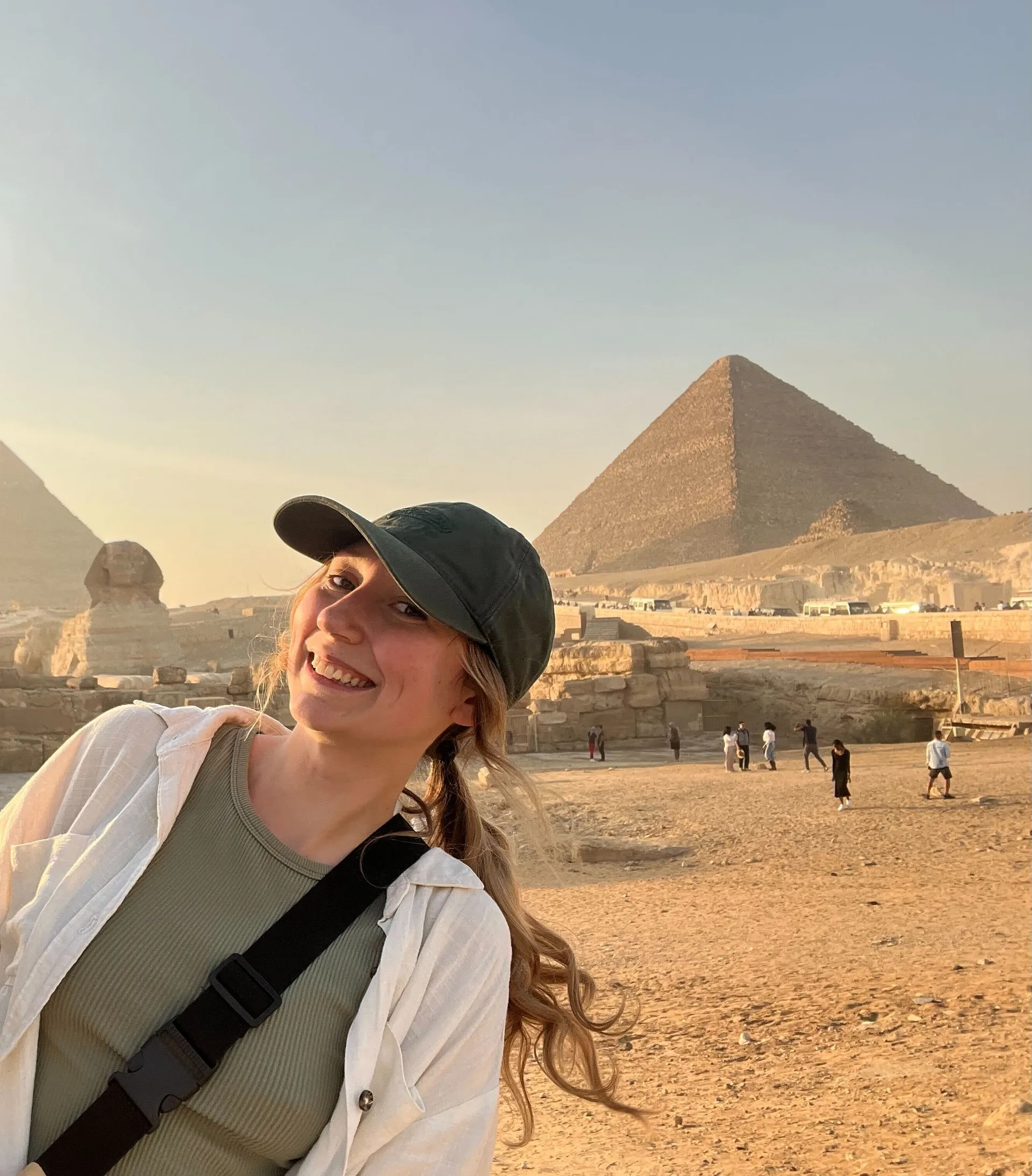 A smiling person stands in front of the Great Pyramid and the Sphinx at the Giza Plateau in Egypt.