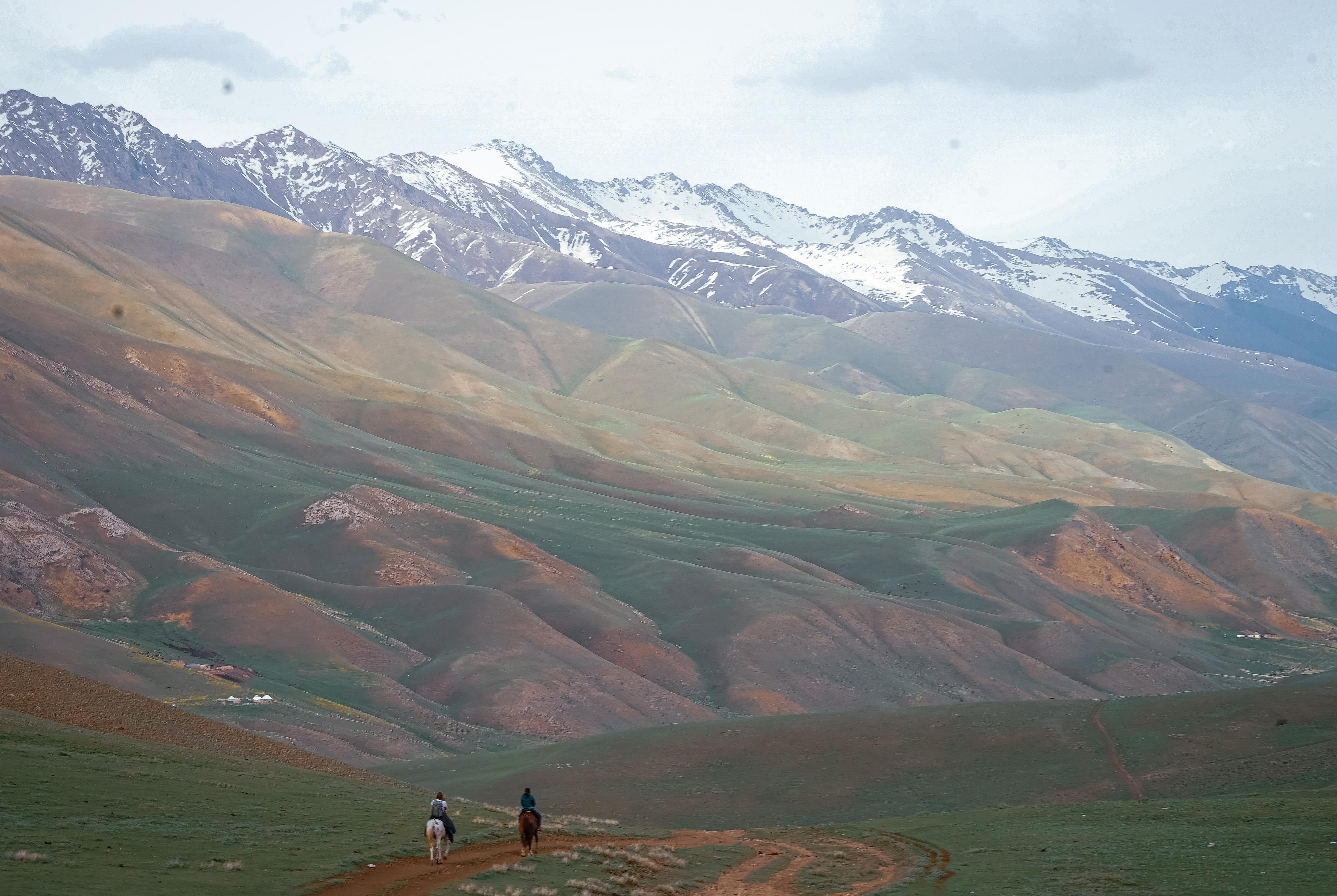 Two horseback riders traverse the rolling hills near the Tian Shan mountains in Kyrgyzstan.