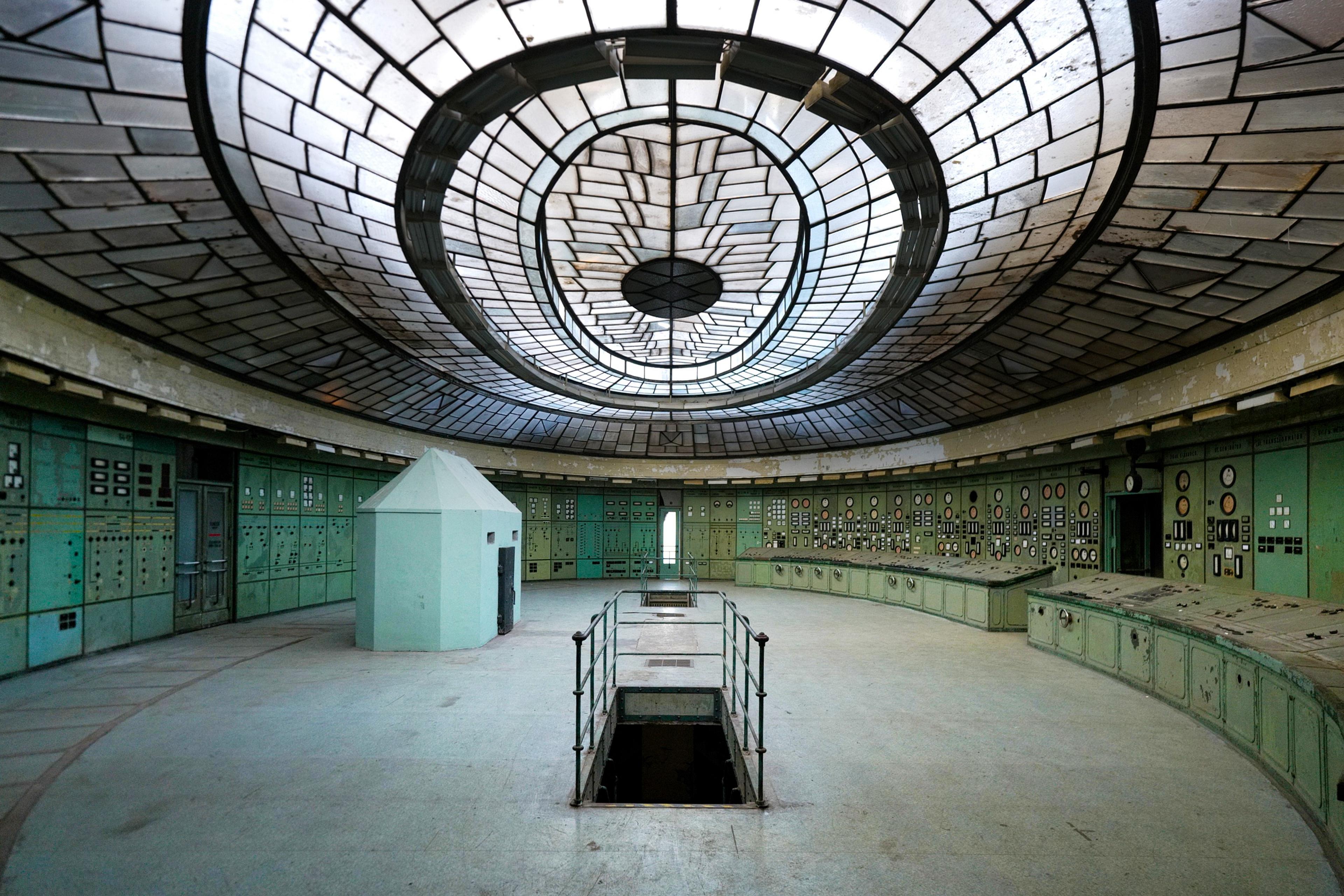 The abandoned control room of Kelenföld Power Plant, featuring rows of vintage dials, switches, and Soviet-era electrical panels under an impressive skylight.