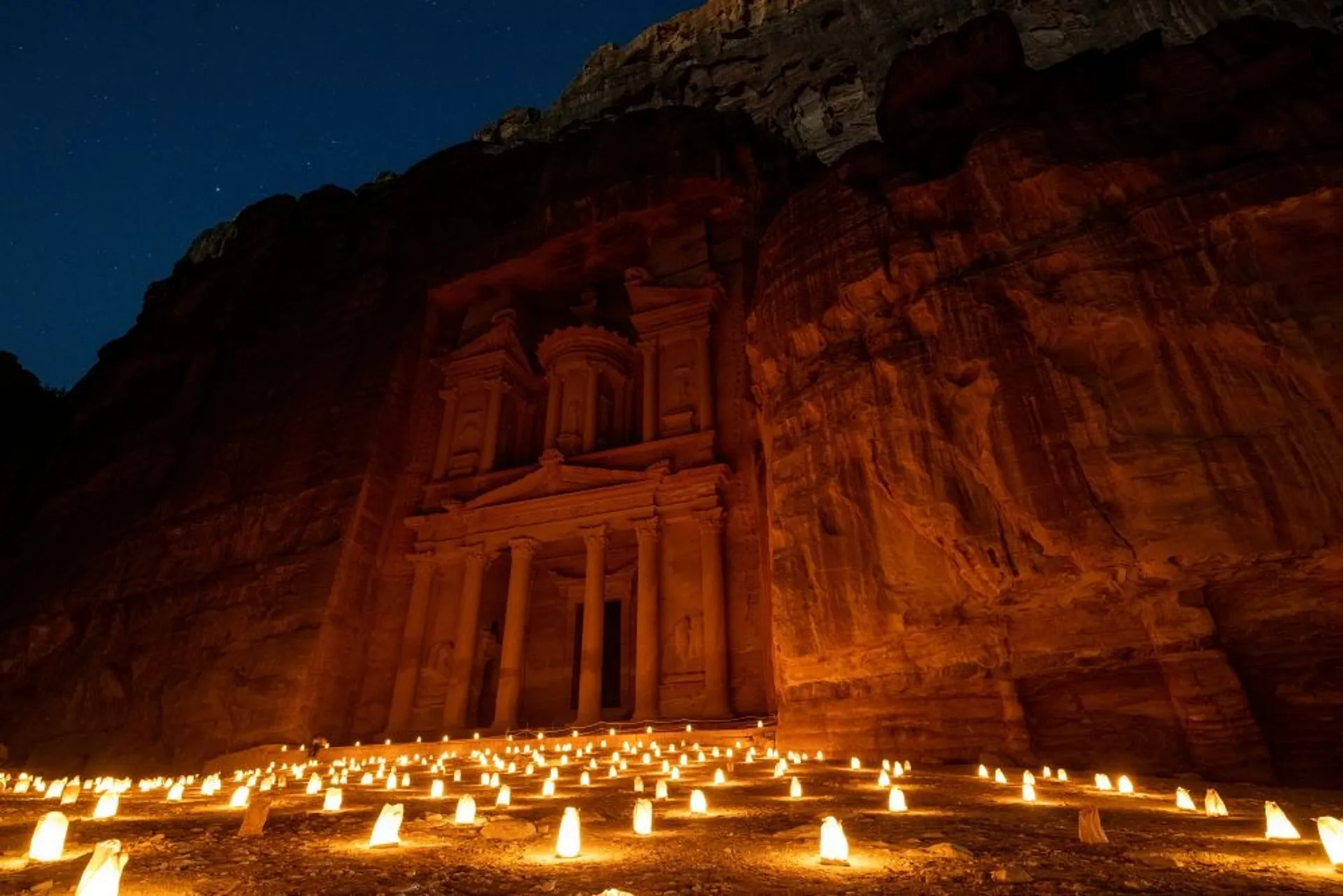 Candles illuminate the ancient rock-carved facade of Al-Khazneh in Petra, Jordan, under a starlit night sky.
