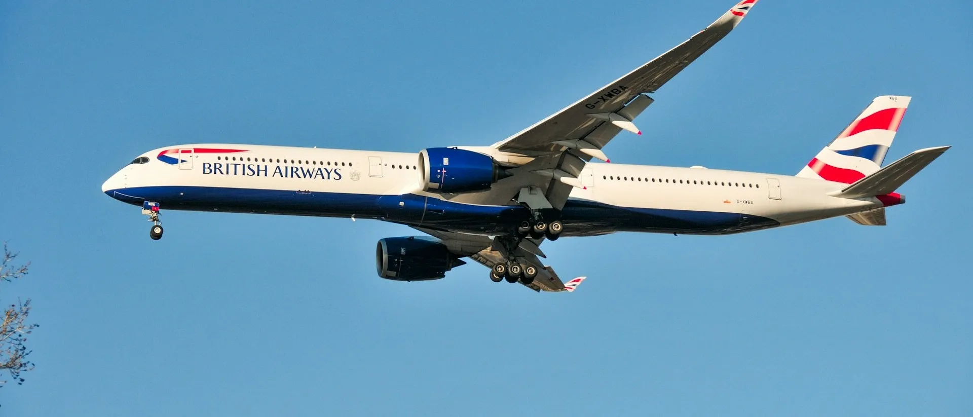 A British Airways plane is captured mid-flight against a clear blue sky, likely on approach or departure at Heathrow Airport in London.