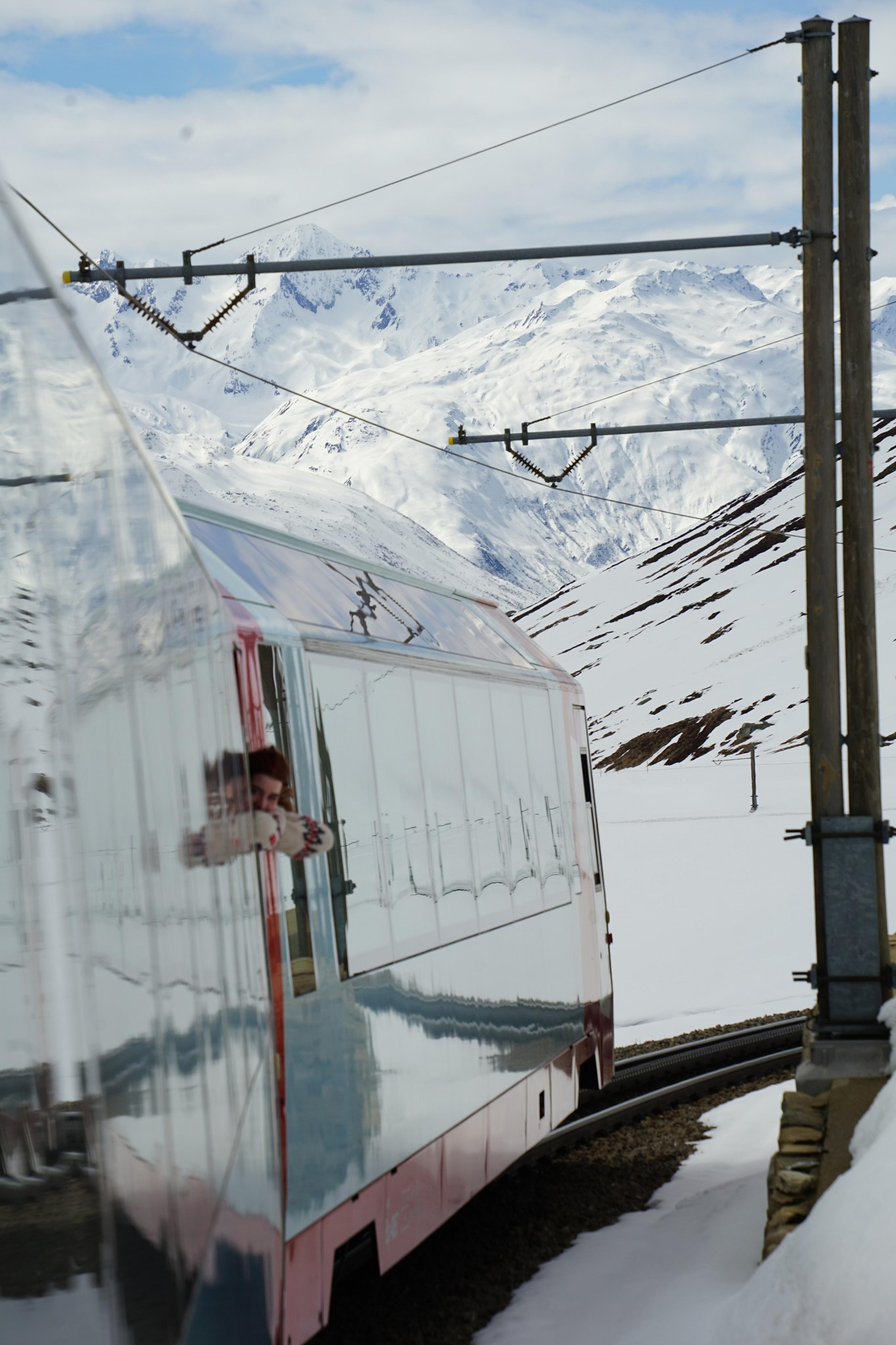 A train reflects snowy peaks as it navigates through the Swiss Alps.