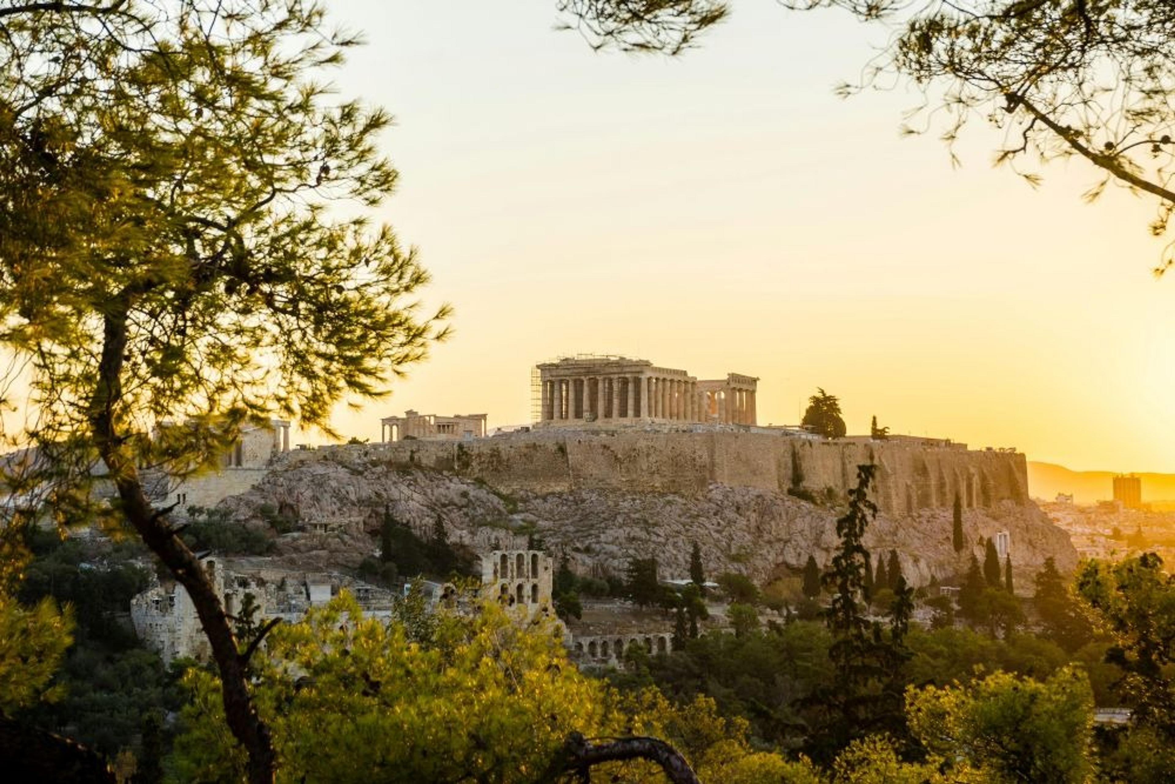 A breathtaking view of the Acropolis in Athens at sunset, framed by lush greenery.