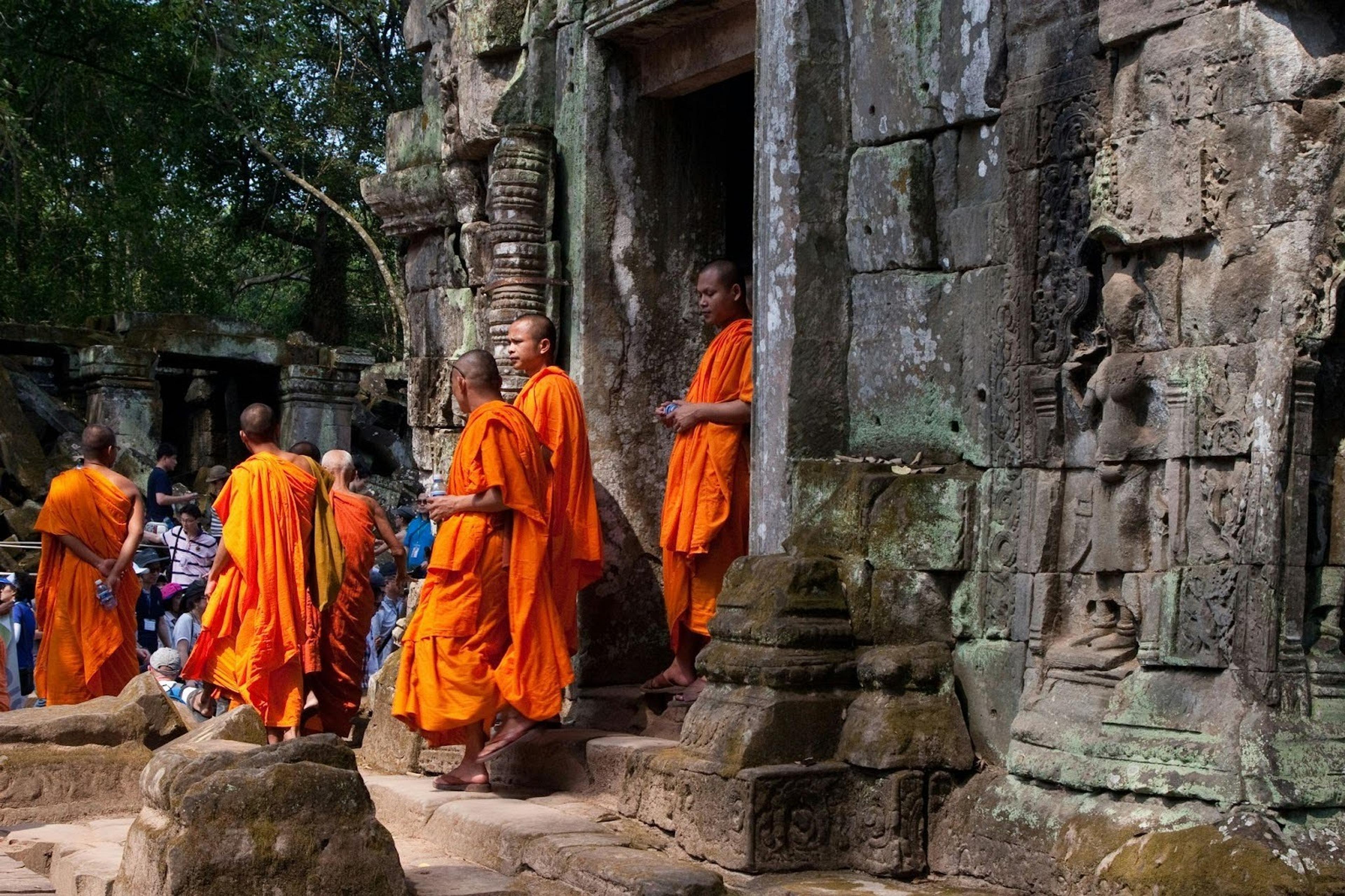 Monks in vibrant orange robes stand among the ancient stone ruins of Angkor Wat, Cambodia.