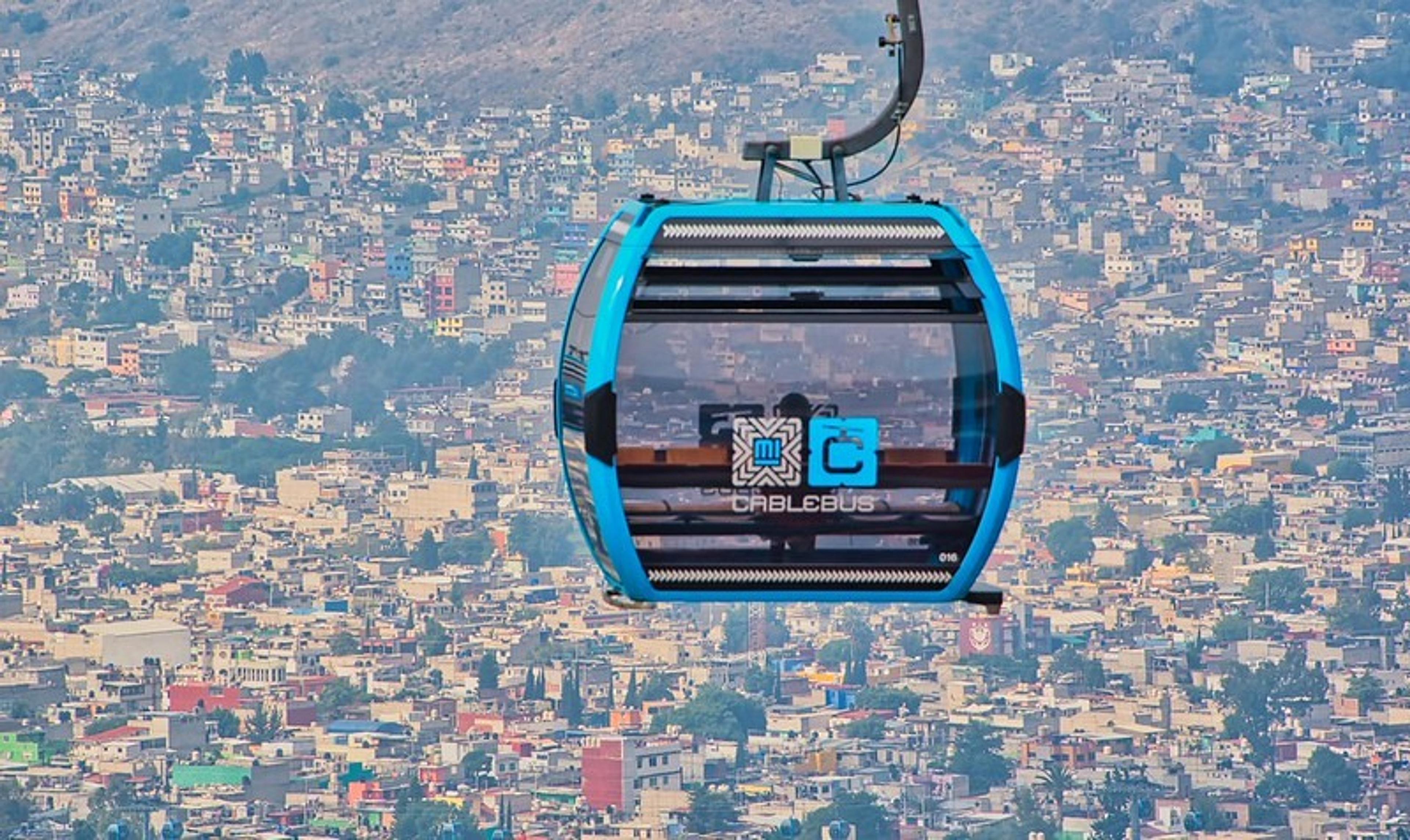A cable car glides over a densely-built area in Mexico City.