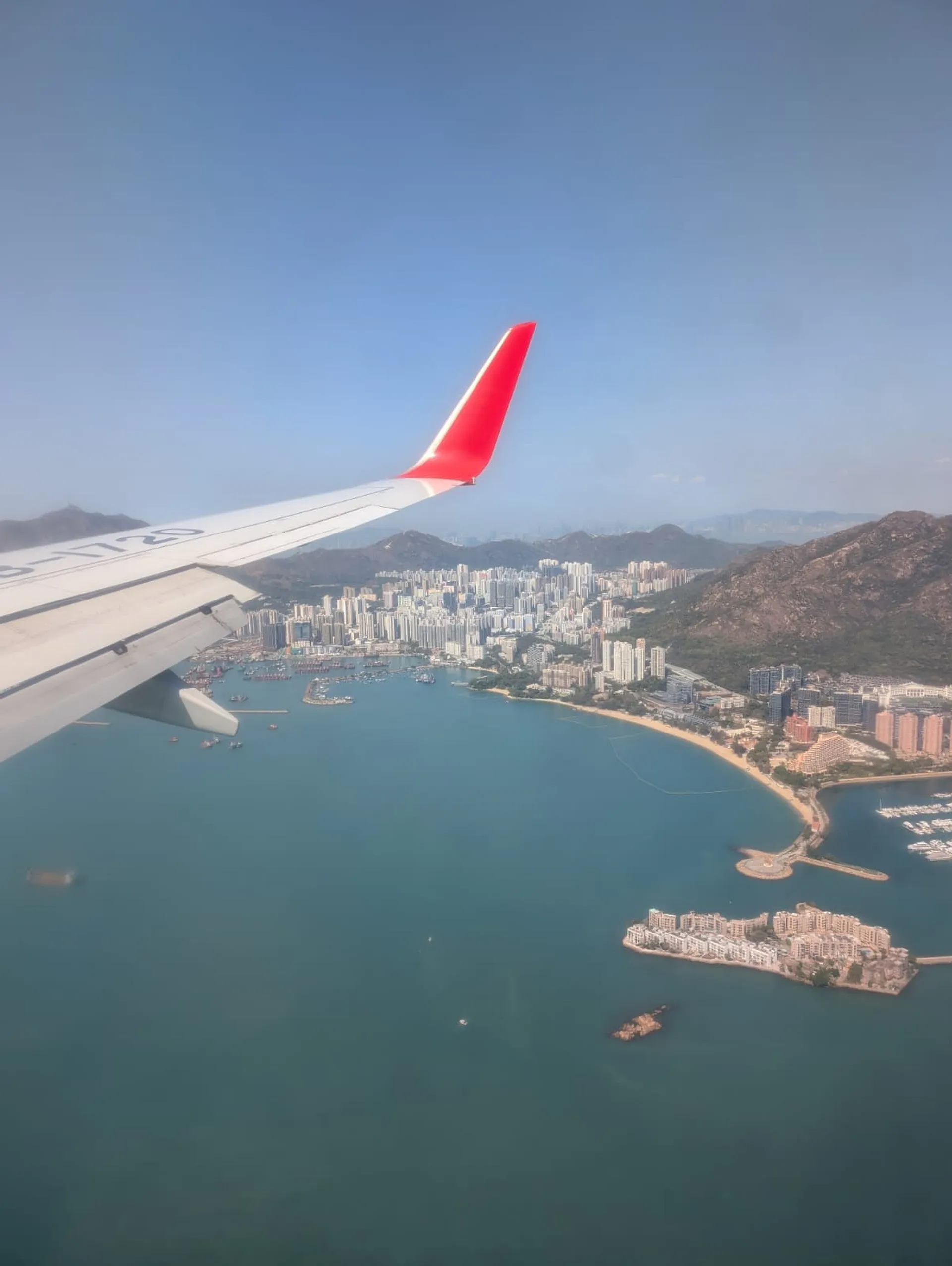 A view of Hong Kong's Tsing Yi Island from a China Eastern airplane window, showcasing skyscrapers, mountains, and the South China Sea.