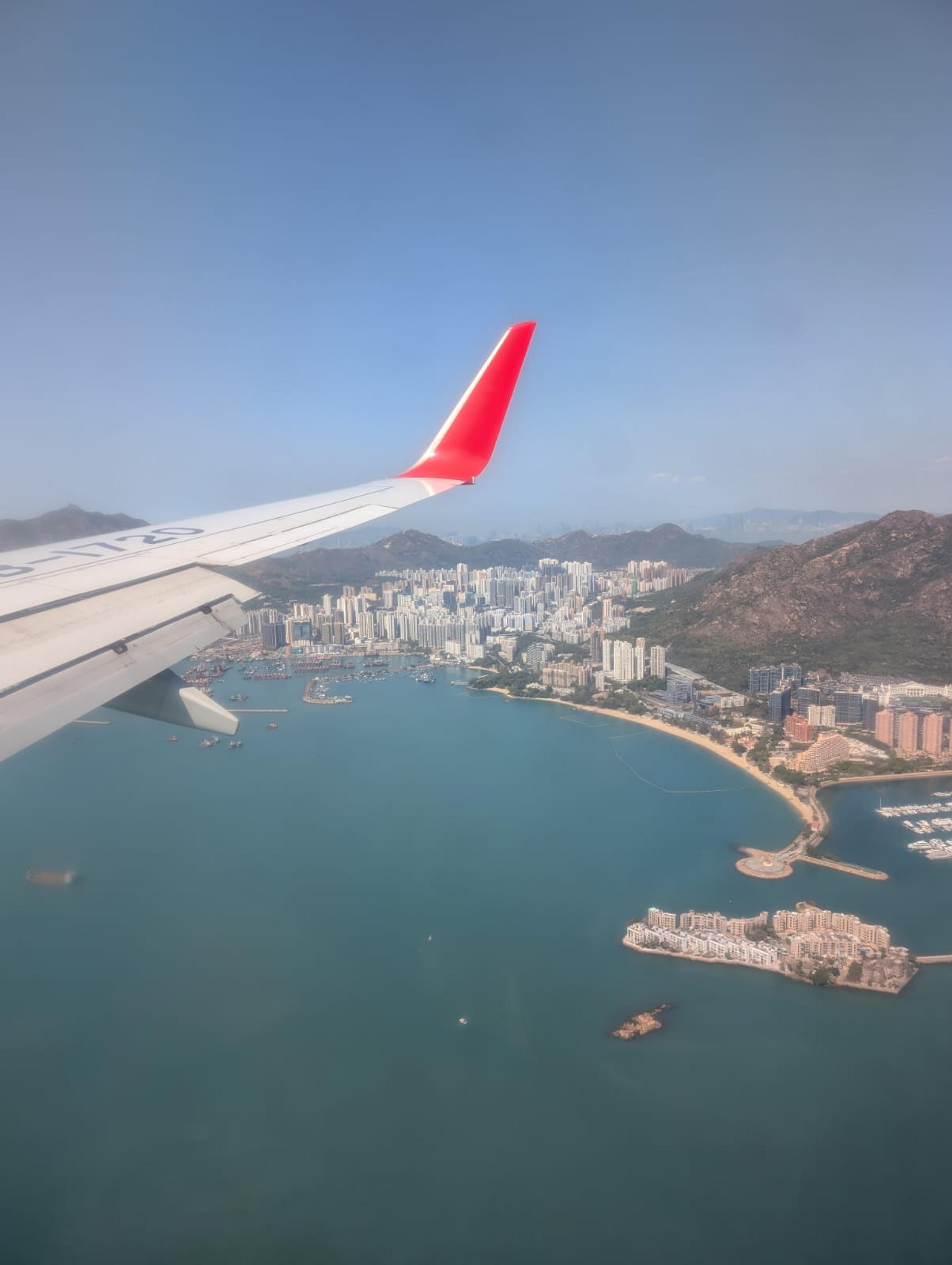 A view of Hong Kong's Tsing Yi Island from a China Eastern airplane window, showcasing skyscrapers, mountains, and the South China Sea.