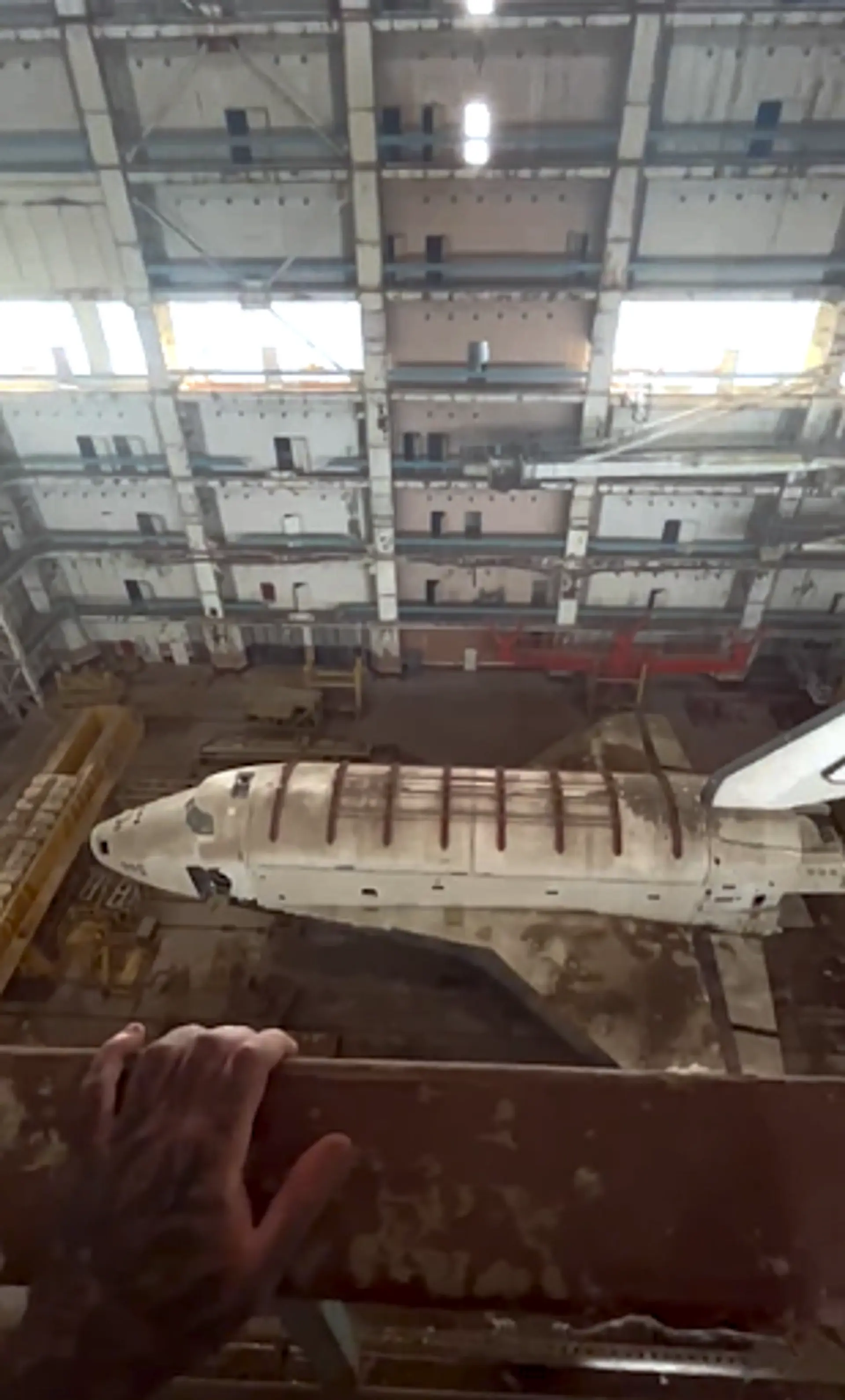 Simon's hand on a railing, looking down at the Soviet space shuttles in Baikonur