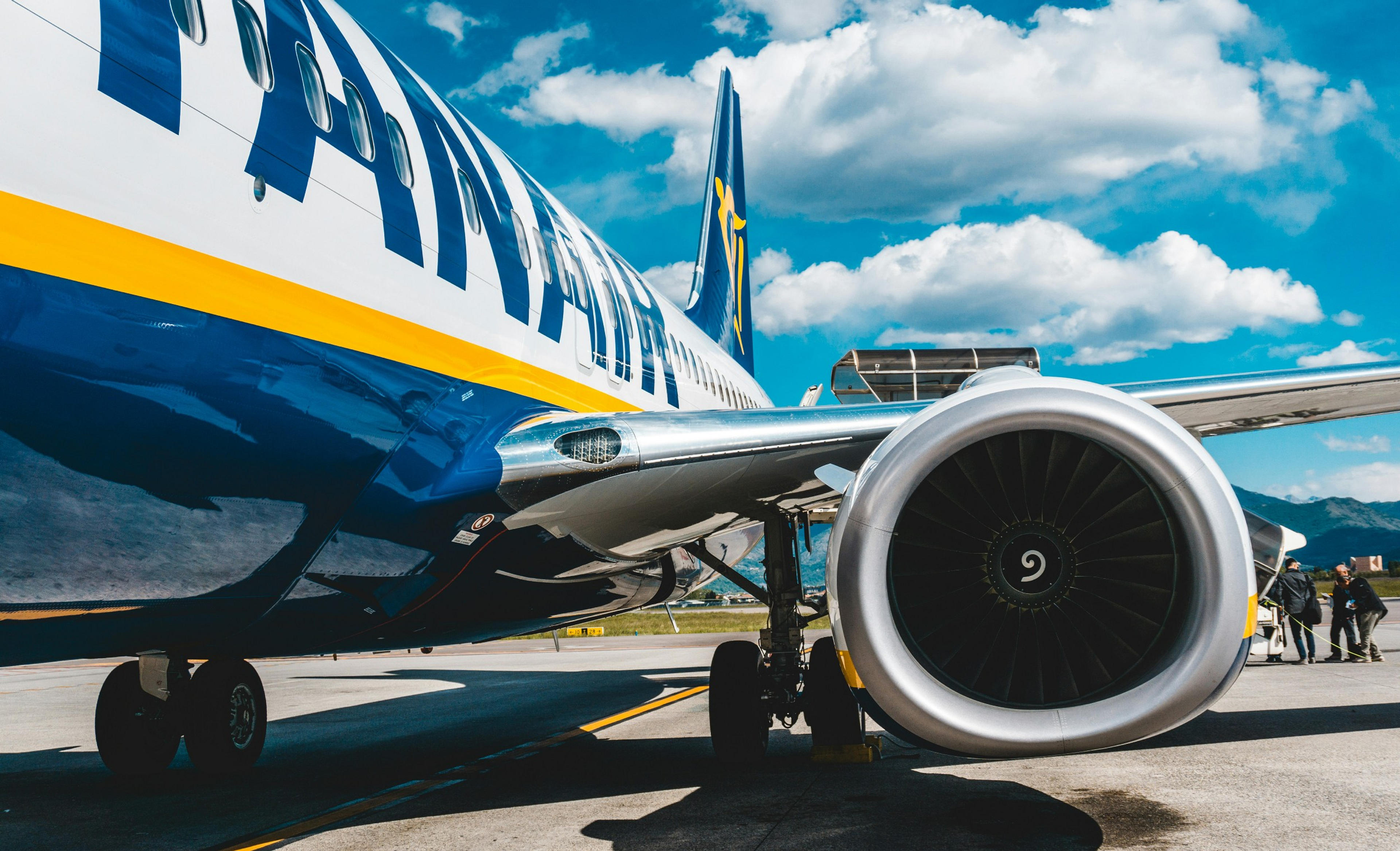 A Ryanair plane is parked on the tarmac at an airport, set against a backdrop of blue skies and fluffy clouds.