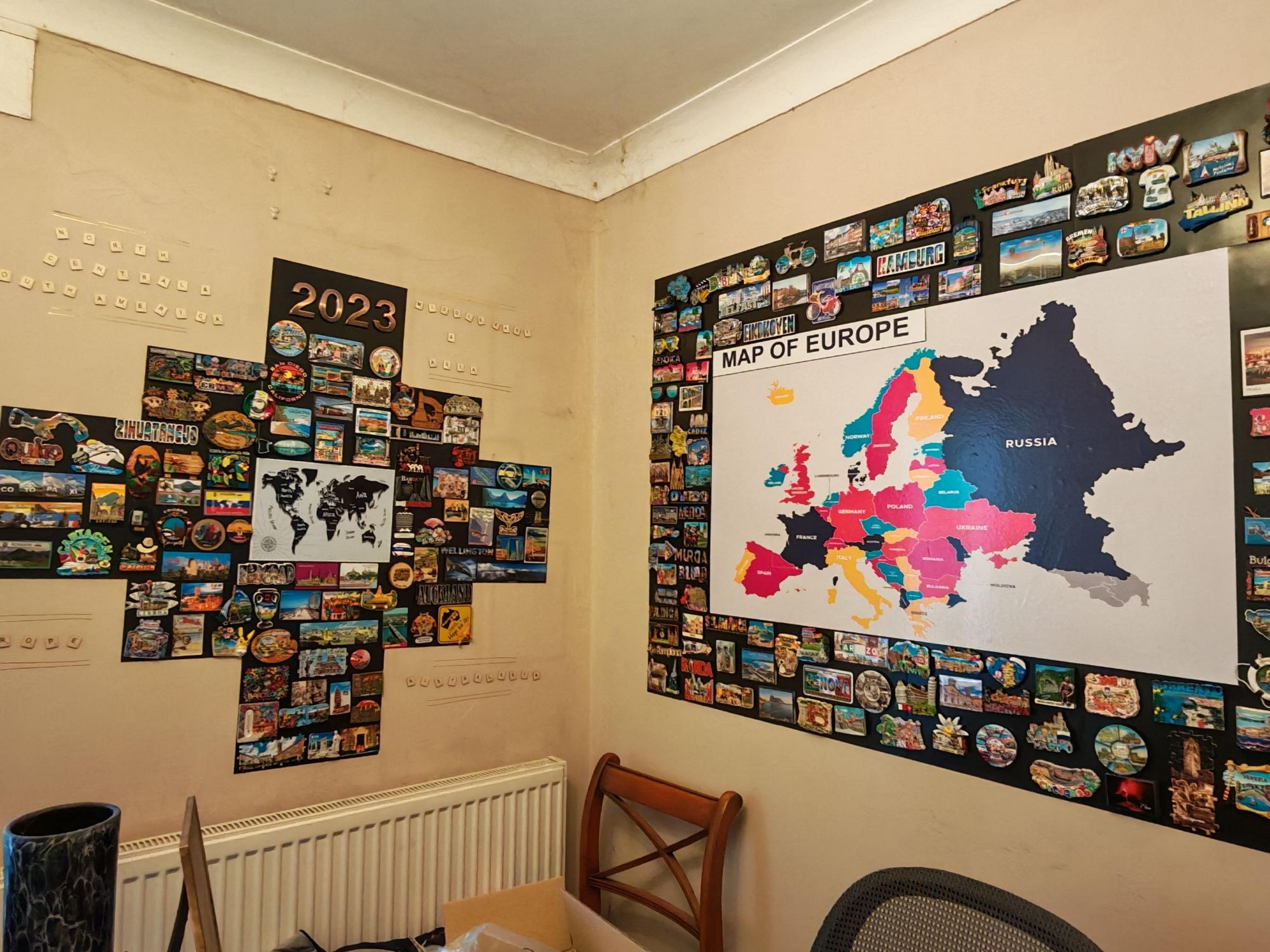 A wall at a home or office is adorned with a colorful "Map of Europe" poster and an array of worldwide postcards and magnets.
