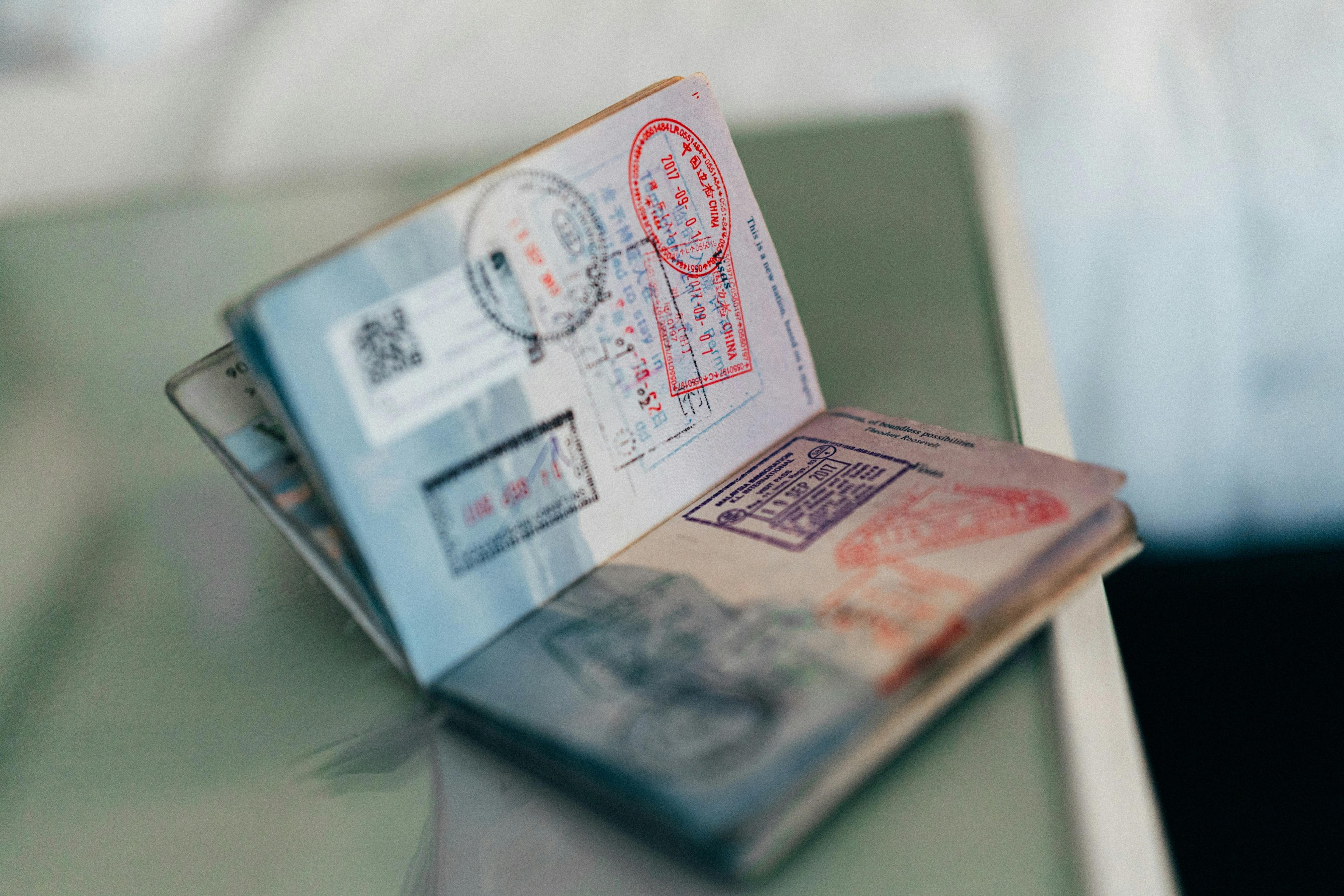 A passport filled with various international stamps, including one from China, rests open on a glass surface.