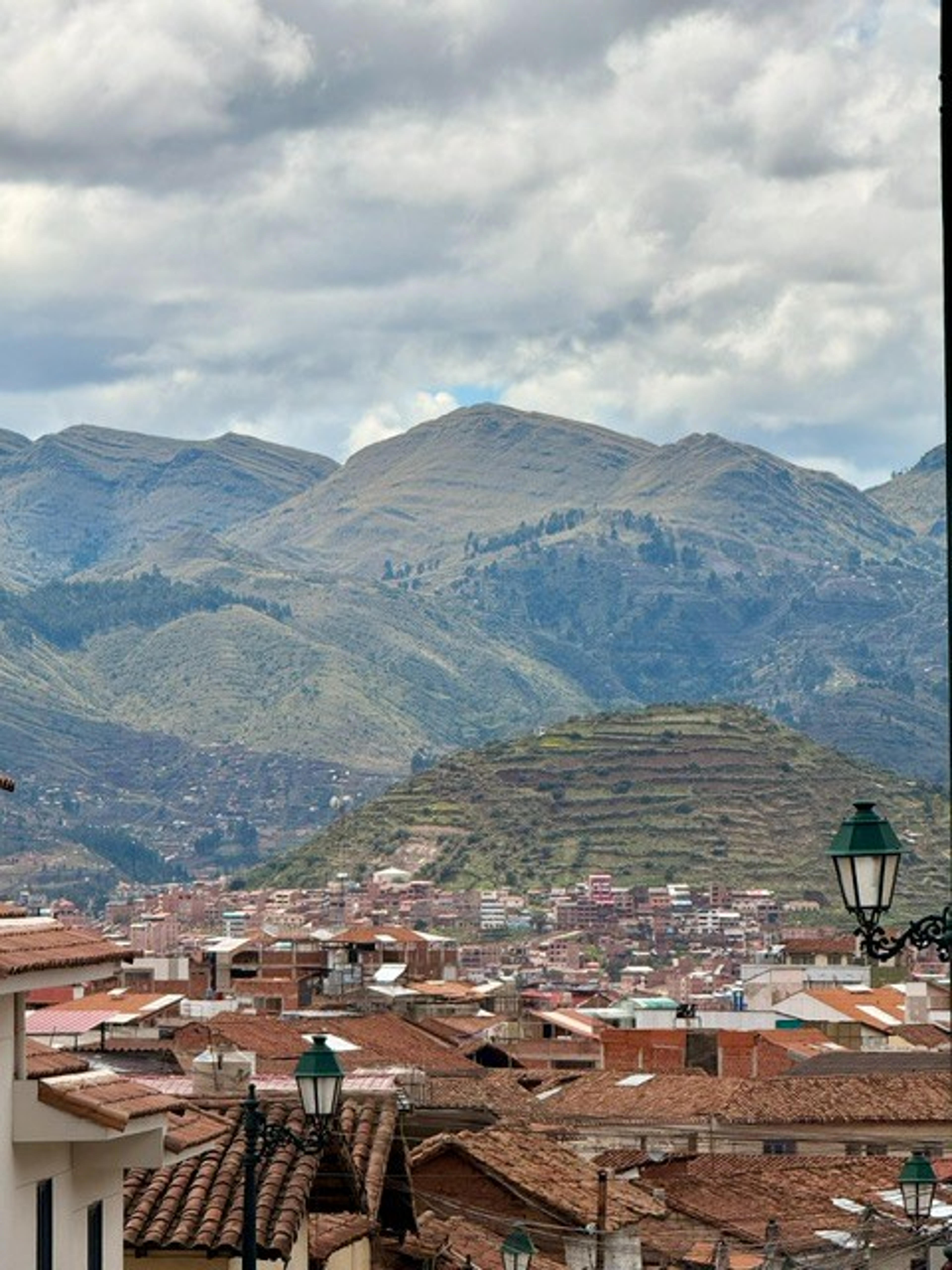 Terracotta rooftops and hilly landscapes surround the city of Ollantaytambo, Peru, with the dramatic Andes mountains as a backdrop.