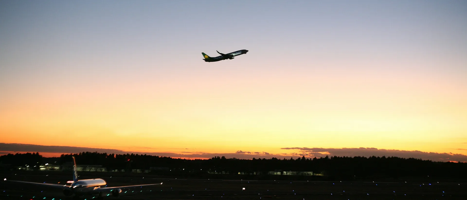 An airplane takes off against a golden sunset at Narita International Airport in Japan.