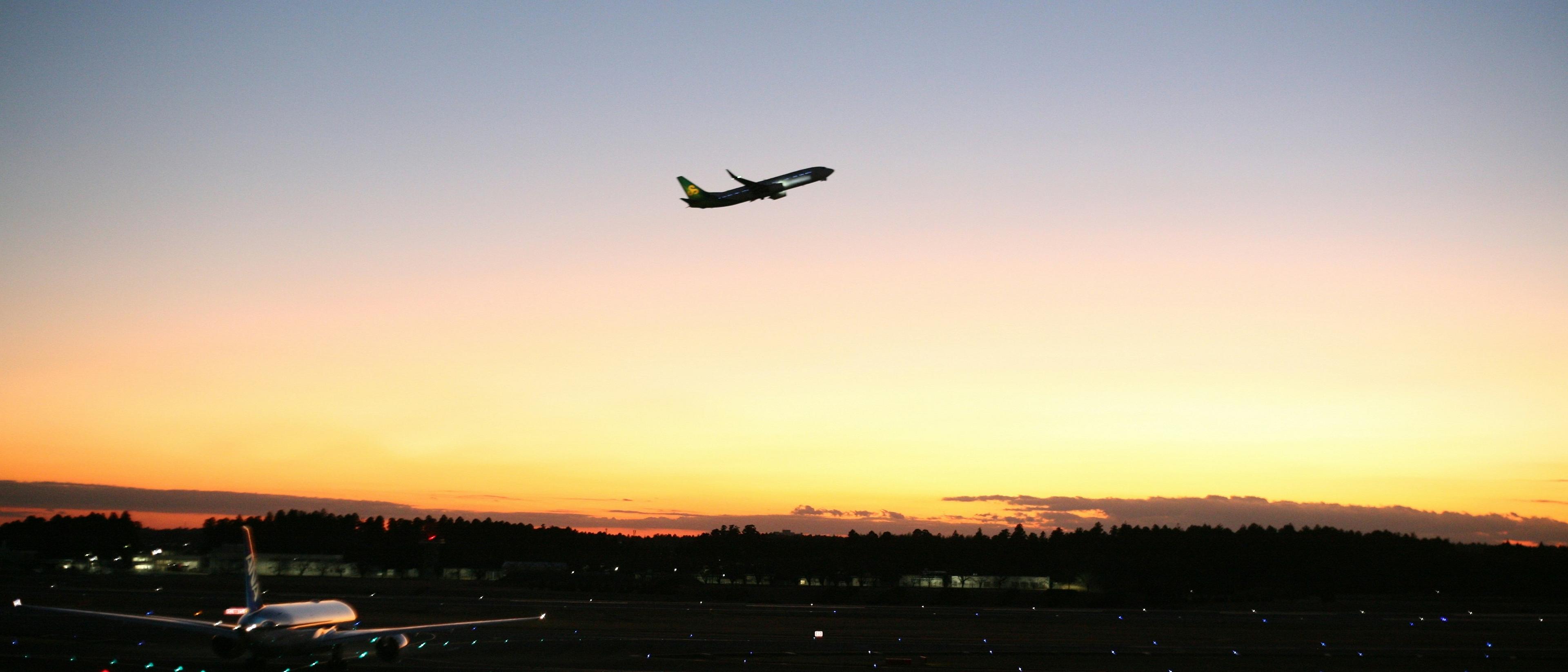 An airplane takes off against a golden sunset at Narita International Airport in Japan.
