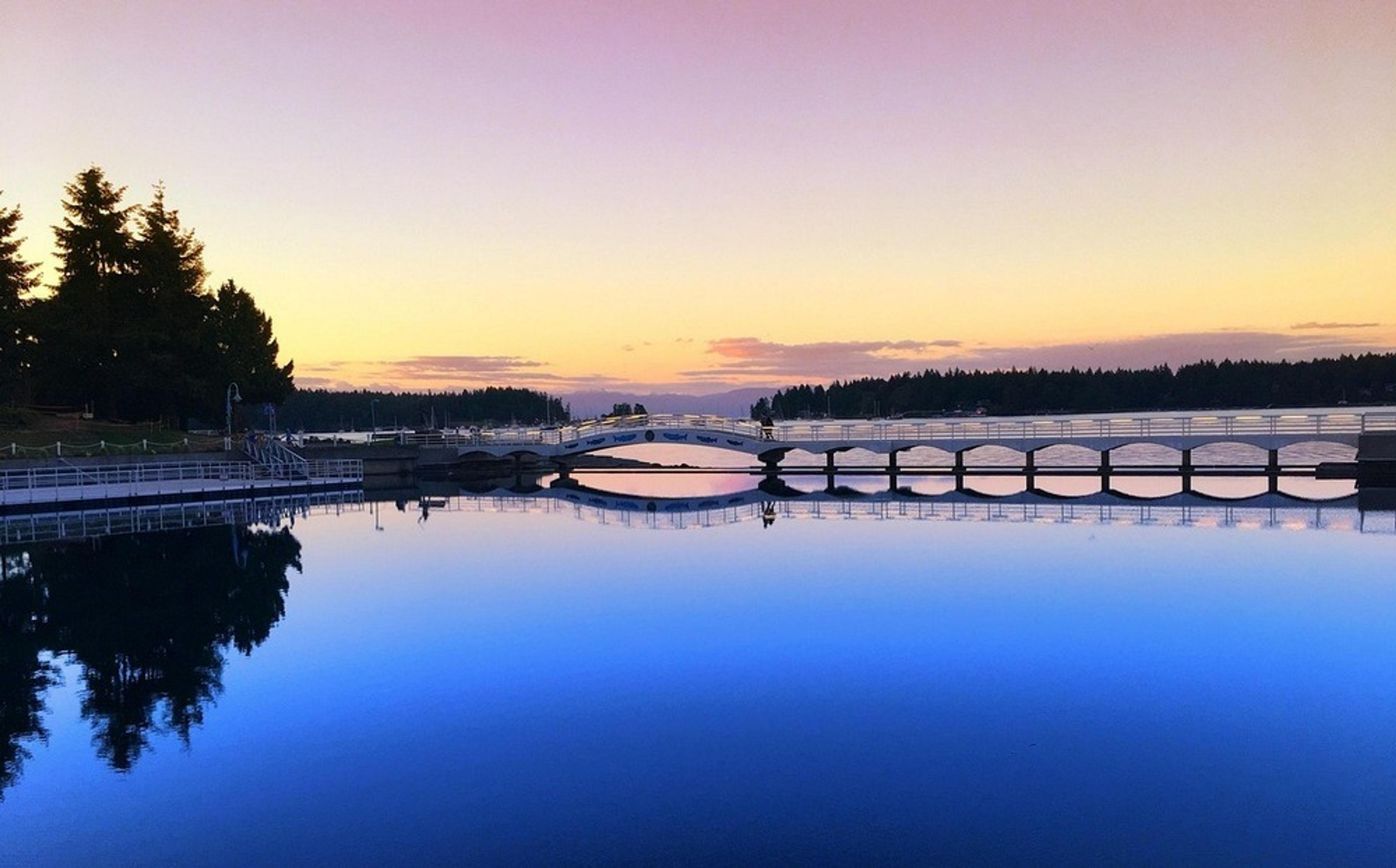 A serene sunset casts a colorful reflection over the iconic wooden bridges spanning the calm waters of Zlatibor Lake in Zlatibor, Serbia.