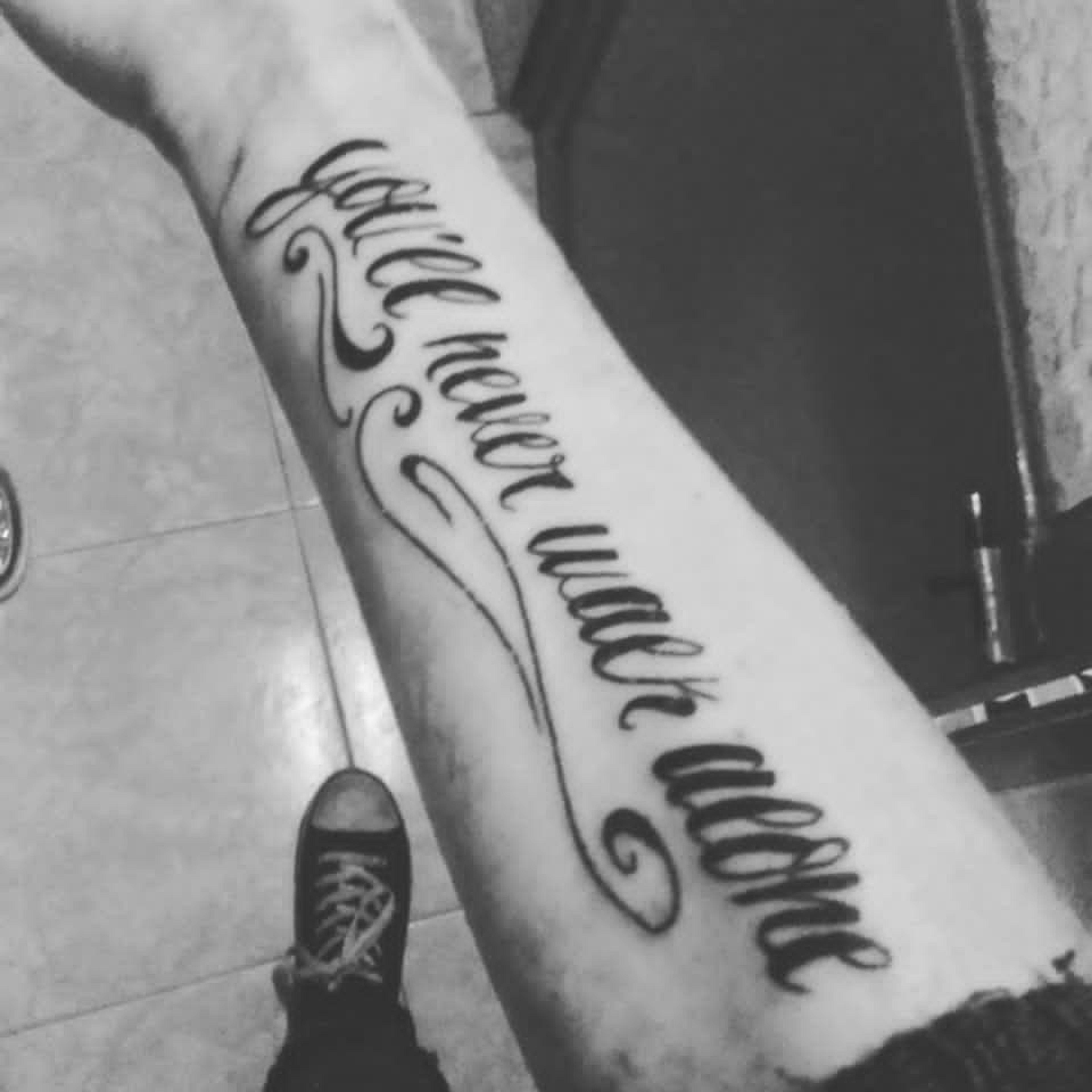 Someone's forearm features a tattoo with the phrase "you'll never walk alone" in stylized script, often associated with Liverpool FC.