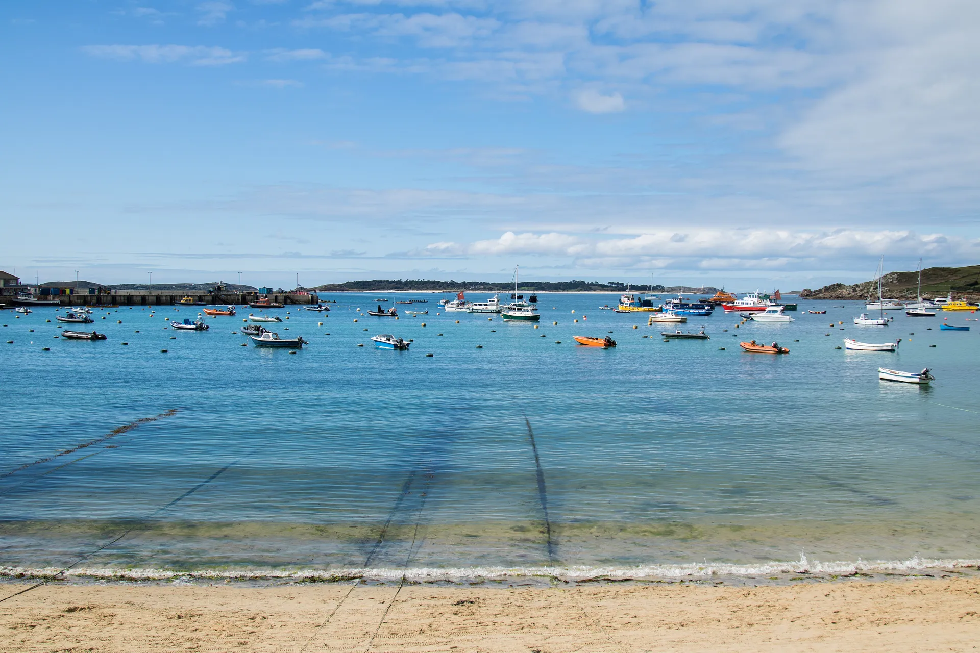 A collection of colorful boats floats on the clear waters of Hugh Town harbour on St Mary's in the Isles of Scilly.