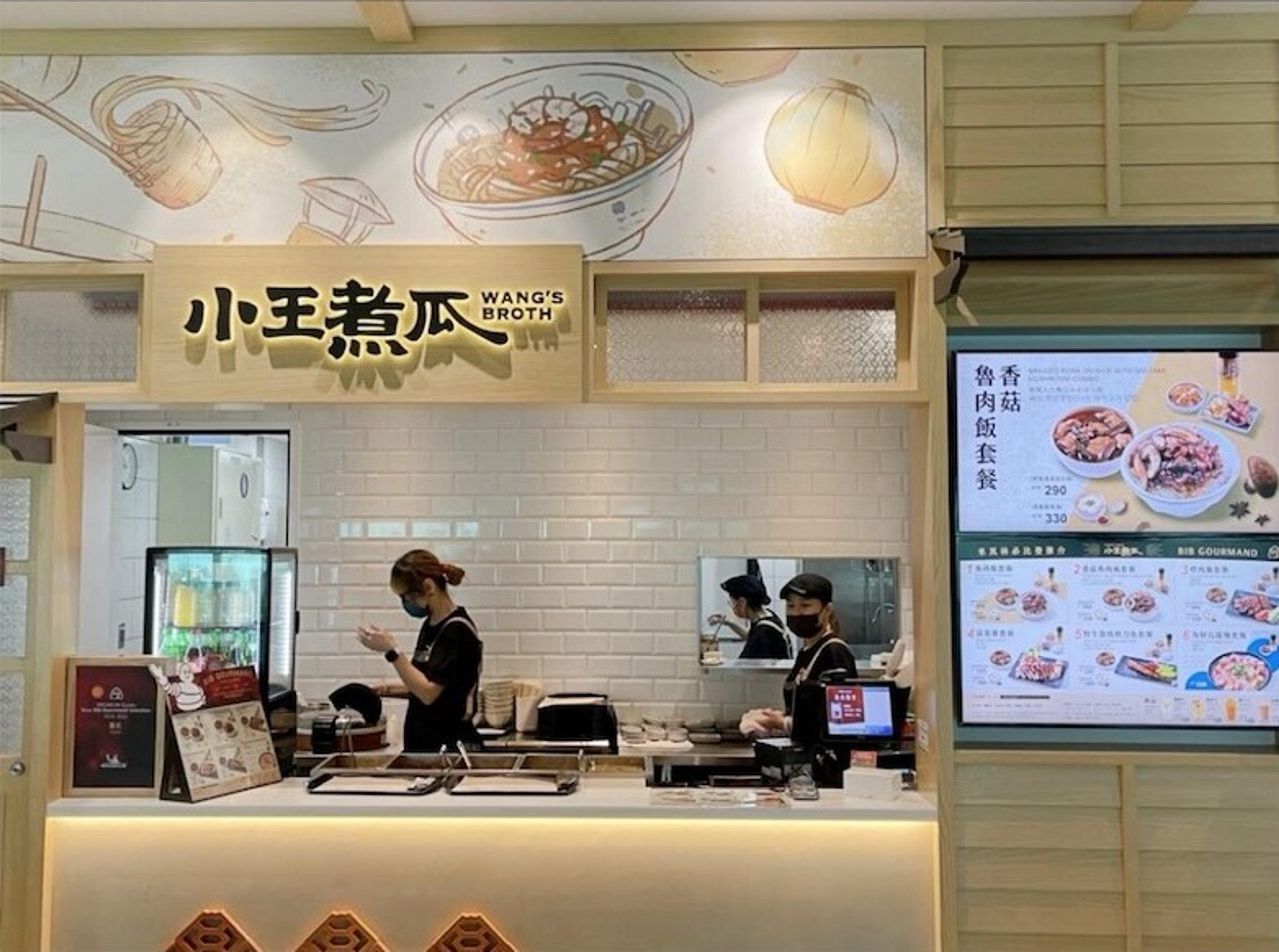 Wang's Broth eatery, identifiable by the signage in Chinese and English, features two workers behind the counter in a modern food outlet setting.
