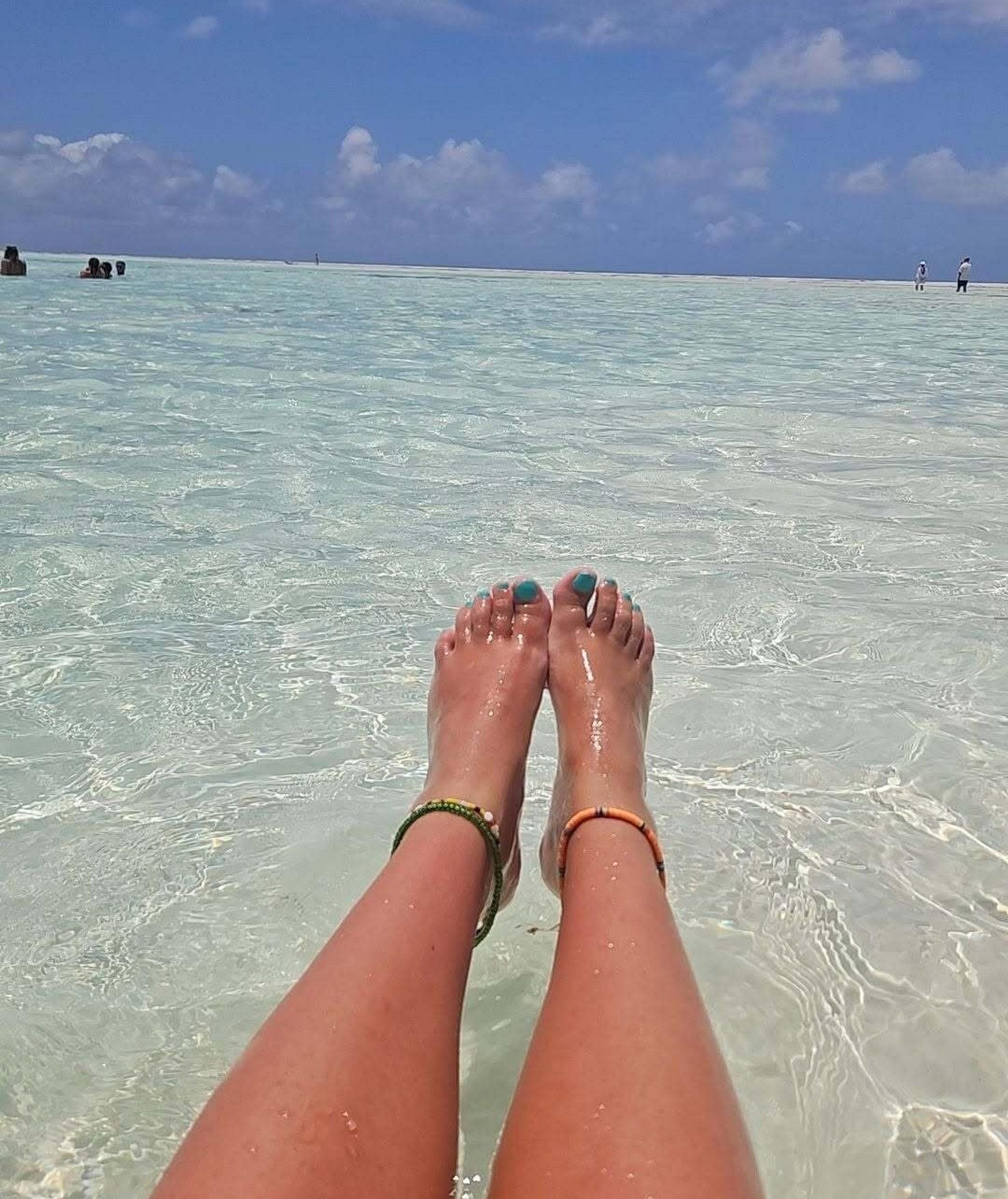 Relaxing in the crystal-clear waters, with anklets adorning sun-kissed legs.