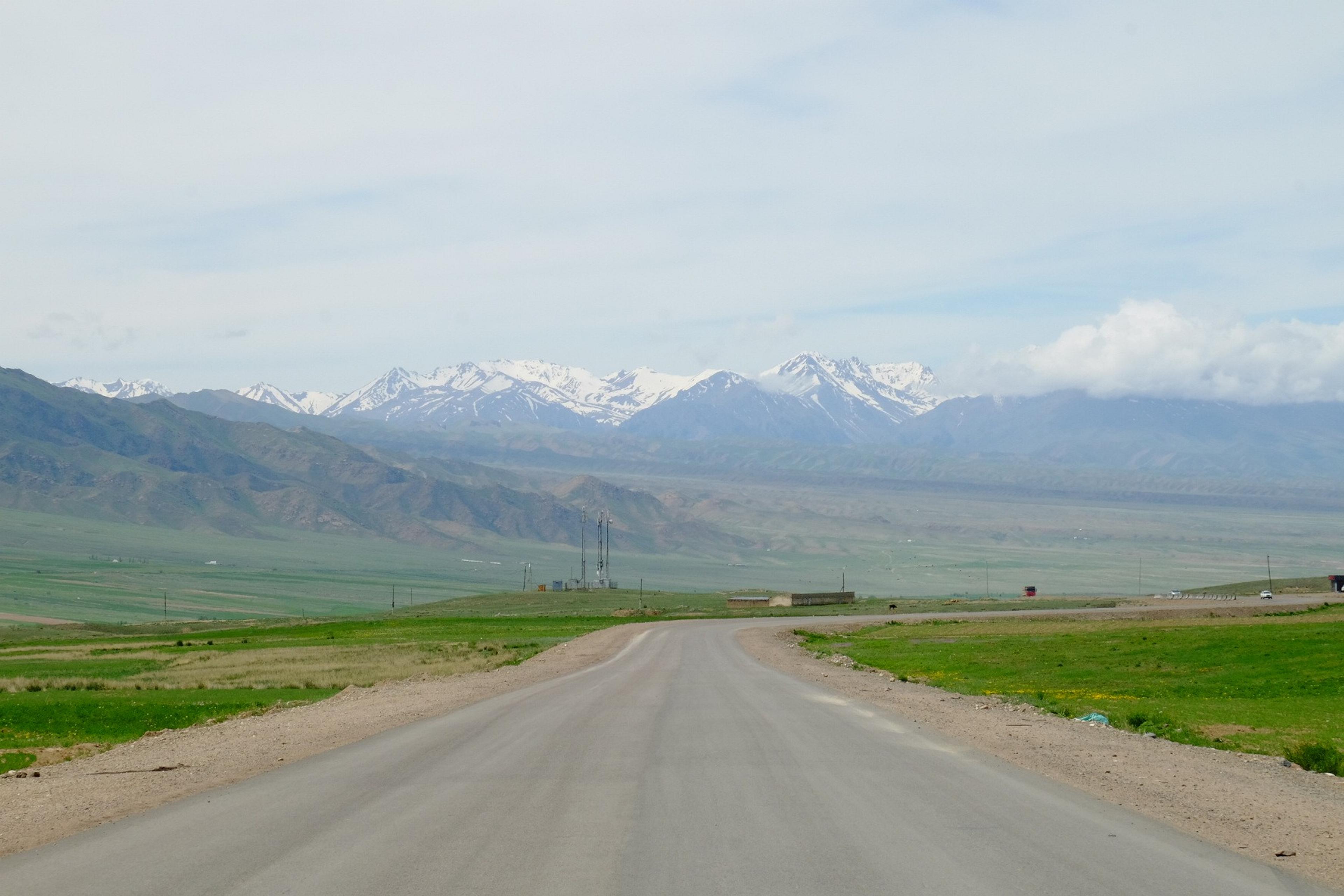 A rural road stretches towards the snow-capped peaks of the Kyrgyz Ala-Too Range in Kyrgyzstan.