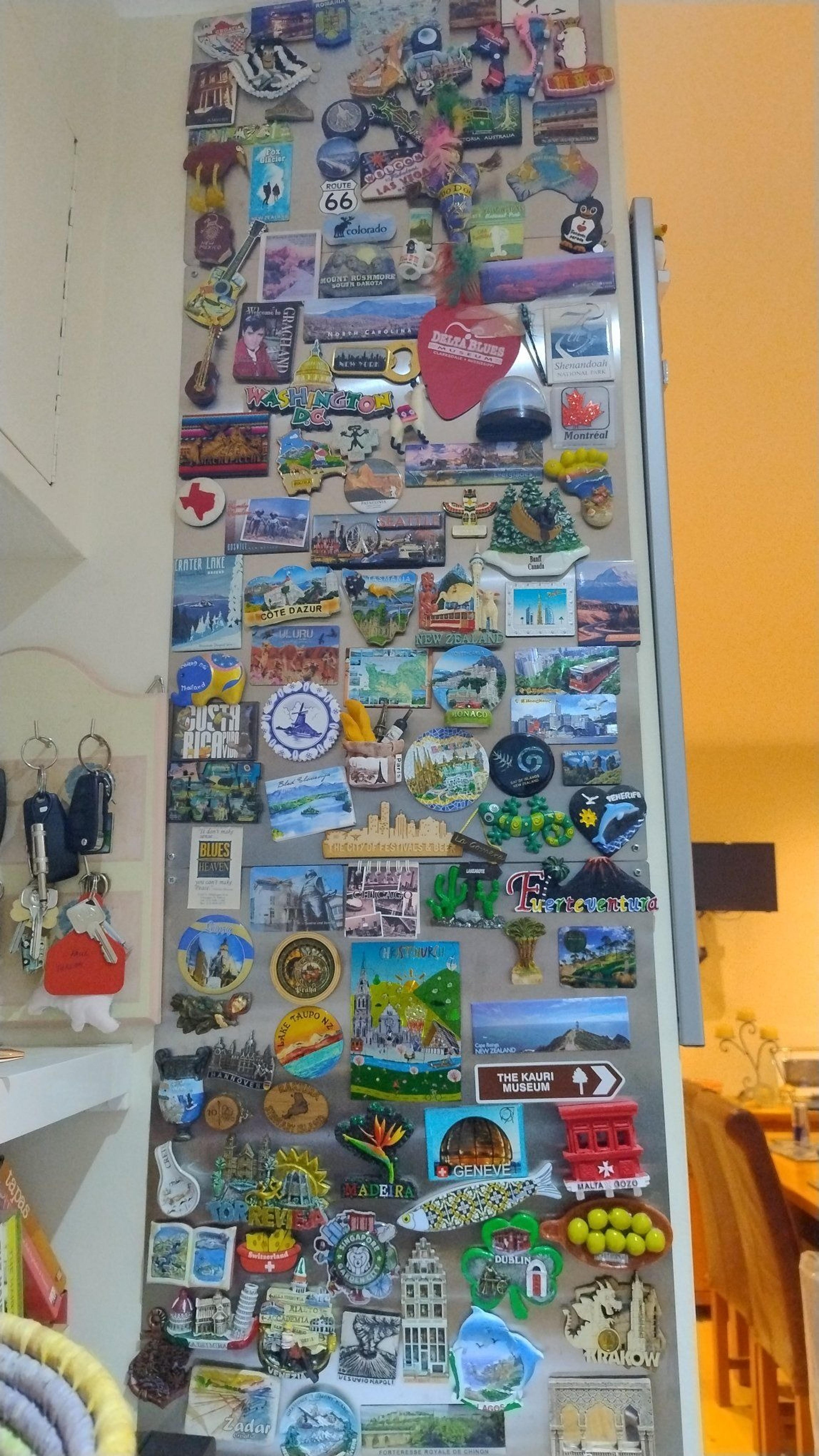 A refrigerator door adorned with a diverse collection of travel magnets from various locations around the world, including Route 66 and Costa Rica.