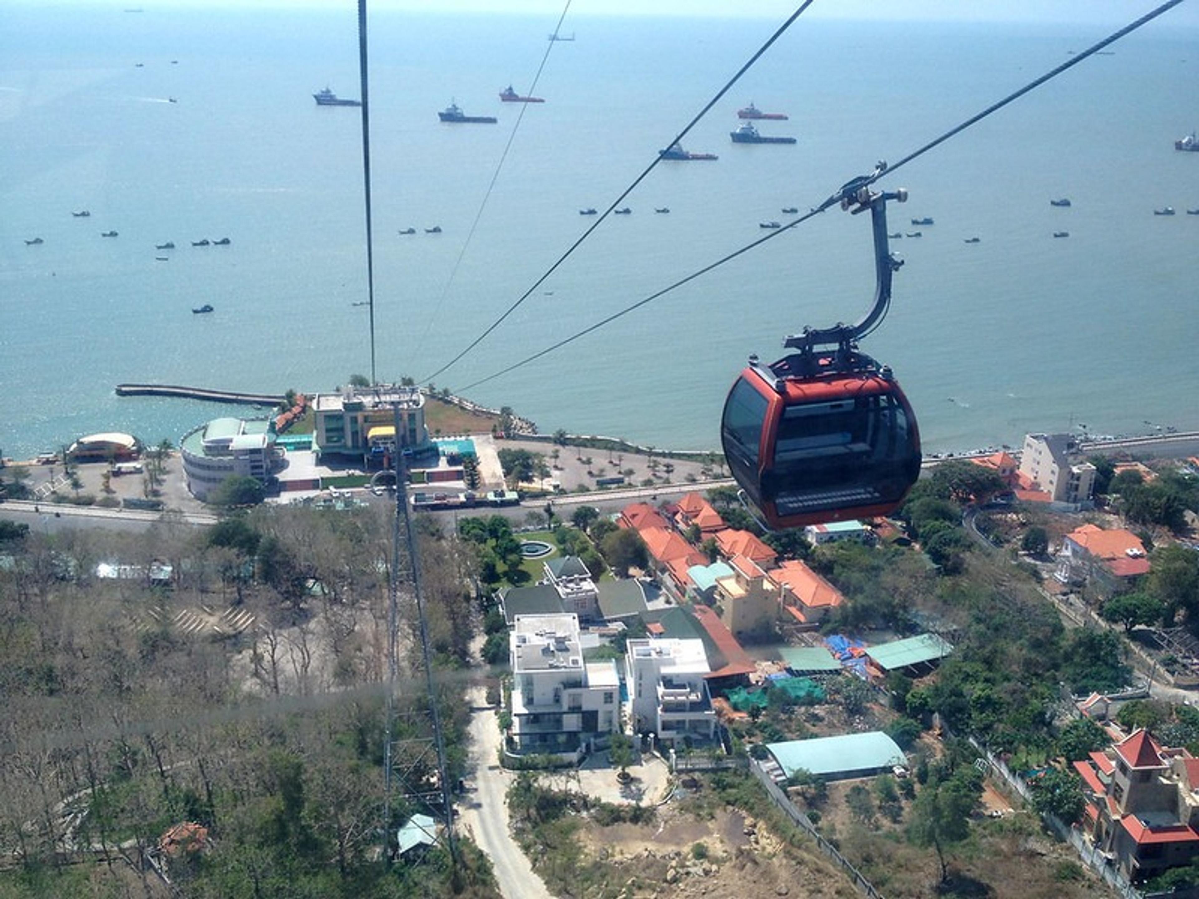 A cable car glides over Vũng Tàu, Vietnam, with ships visible in the distant ocean.