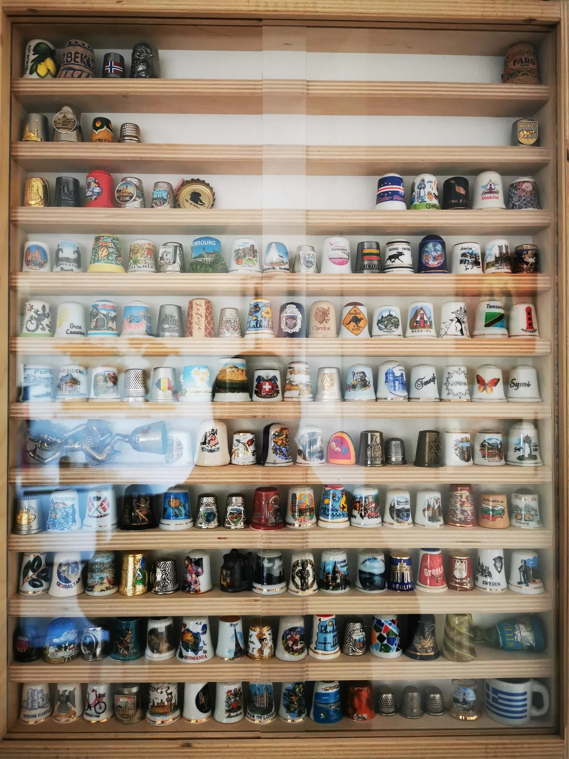 A display case filled with souvenir thimbles, each representing different locations around the world, including Berlin and Crete.