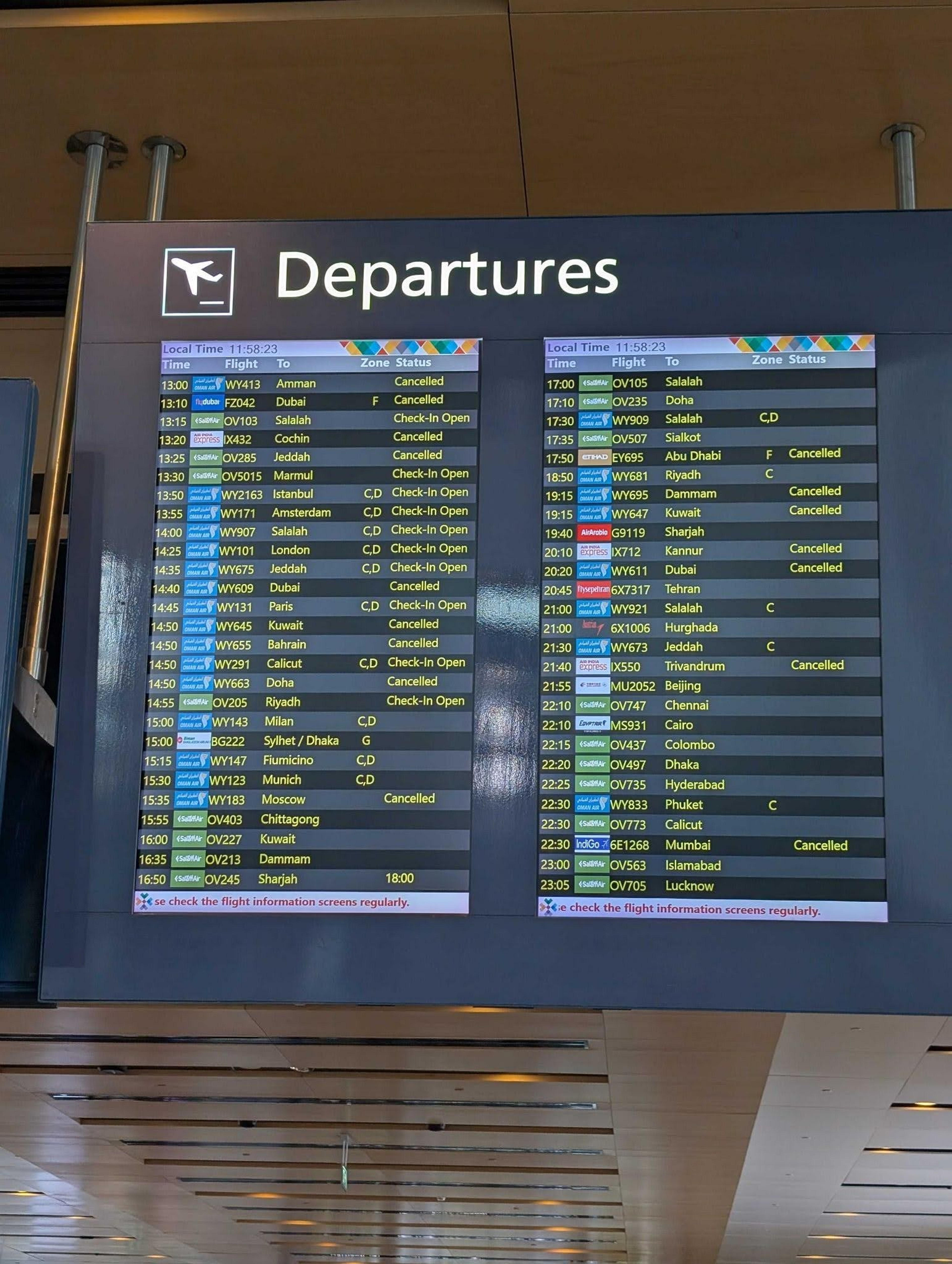 A departures board at Muscat International Airport displays flight status information.