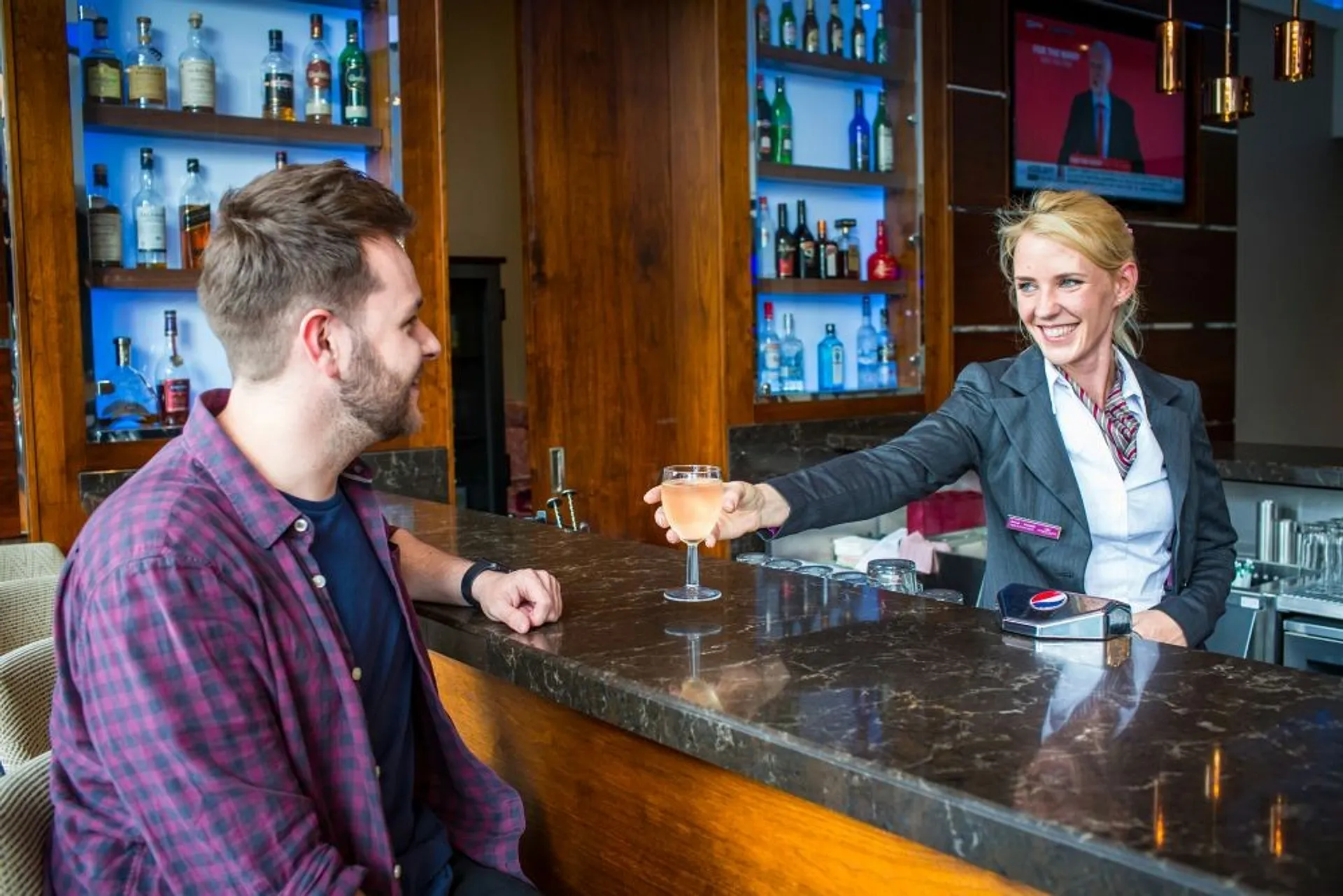 A bartender serves a drink to a customer at a marble countertop in a stylish Gatwick Airport bar.