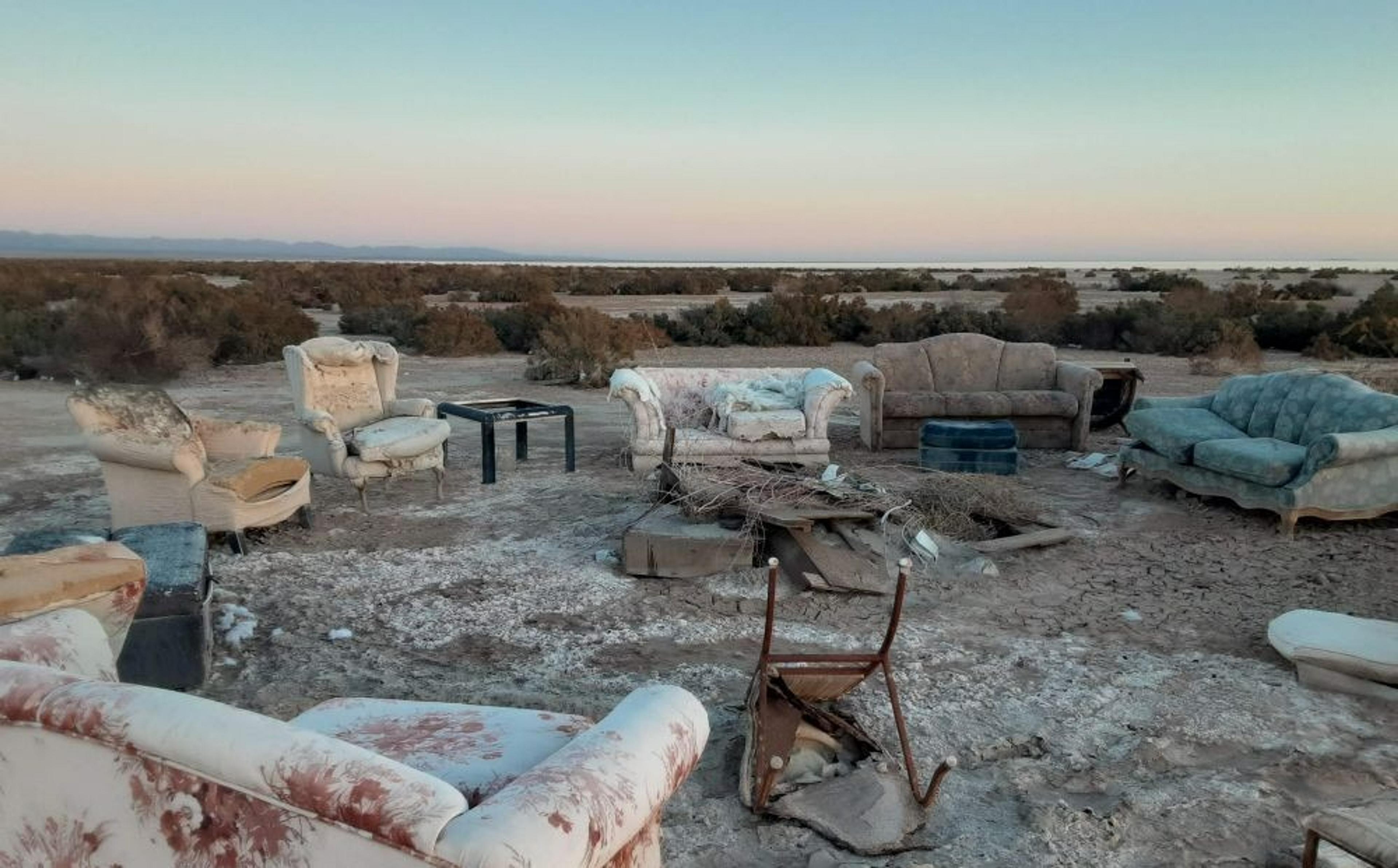 A collection of weathered sofas and chairs is arranged in a circle on the cracked desert floor near the Salton Sea in California.