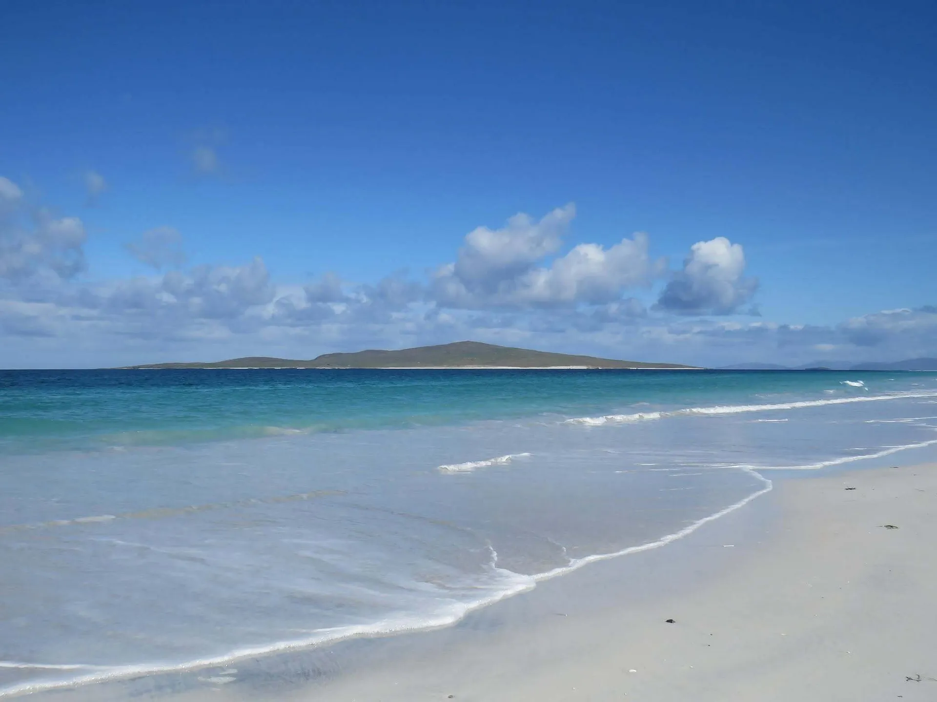 A tranquil beach with white sand and turquoise waters stretches out on Berneray Island in the Outer Hebrides, Scotland.