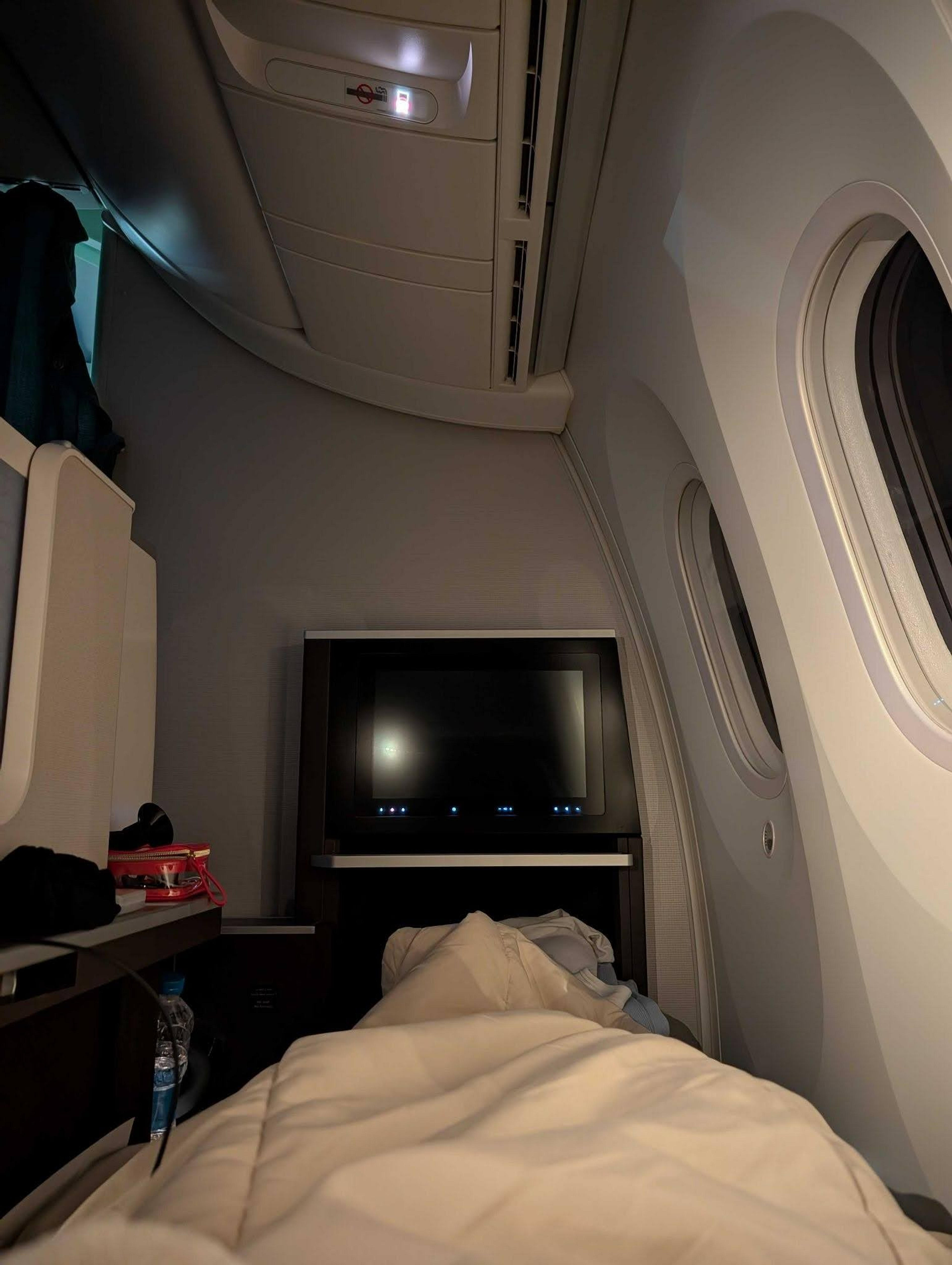 A cozy first-class cabin in an airplane, featuring a flat-screen TV and plush bedding, offers a luxurious travel experience.
