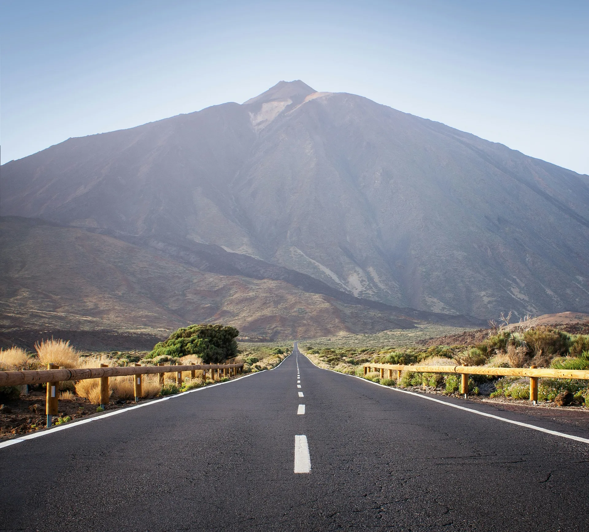 A road leads towards the imposing Mount Teide on Tenerife, framed by rugged terrain under a clear sky.