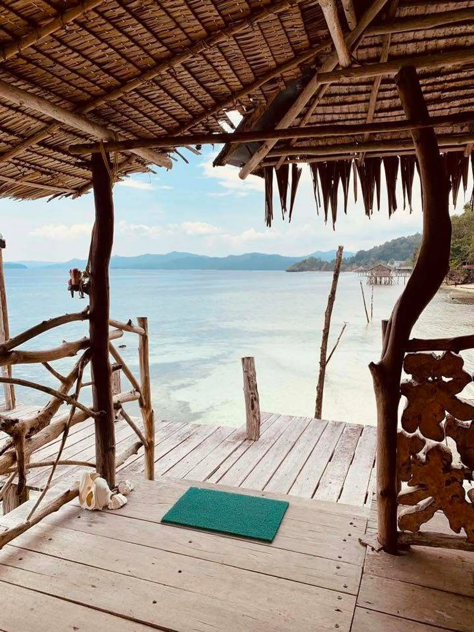 A rustic wooden pavilion overlooks the tranquil waters of a coastal area in Southeast Asia, possibly hinting at a serene island retreat.