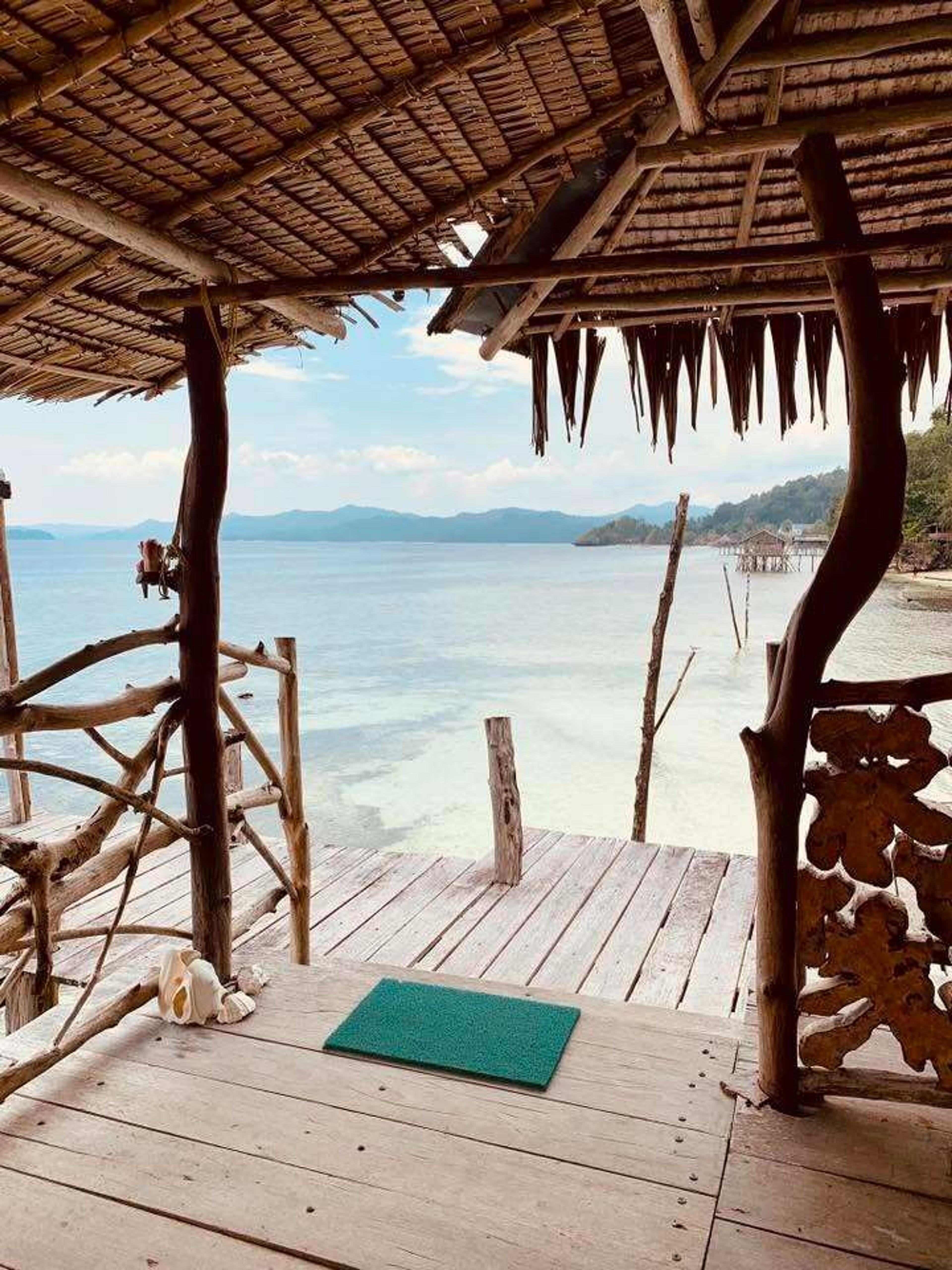 A rustic wooden pavilion overlooks the tranquil waters of a coastal area in Southeast Asia, possibly hinting at a serene island retreat.