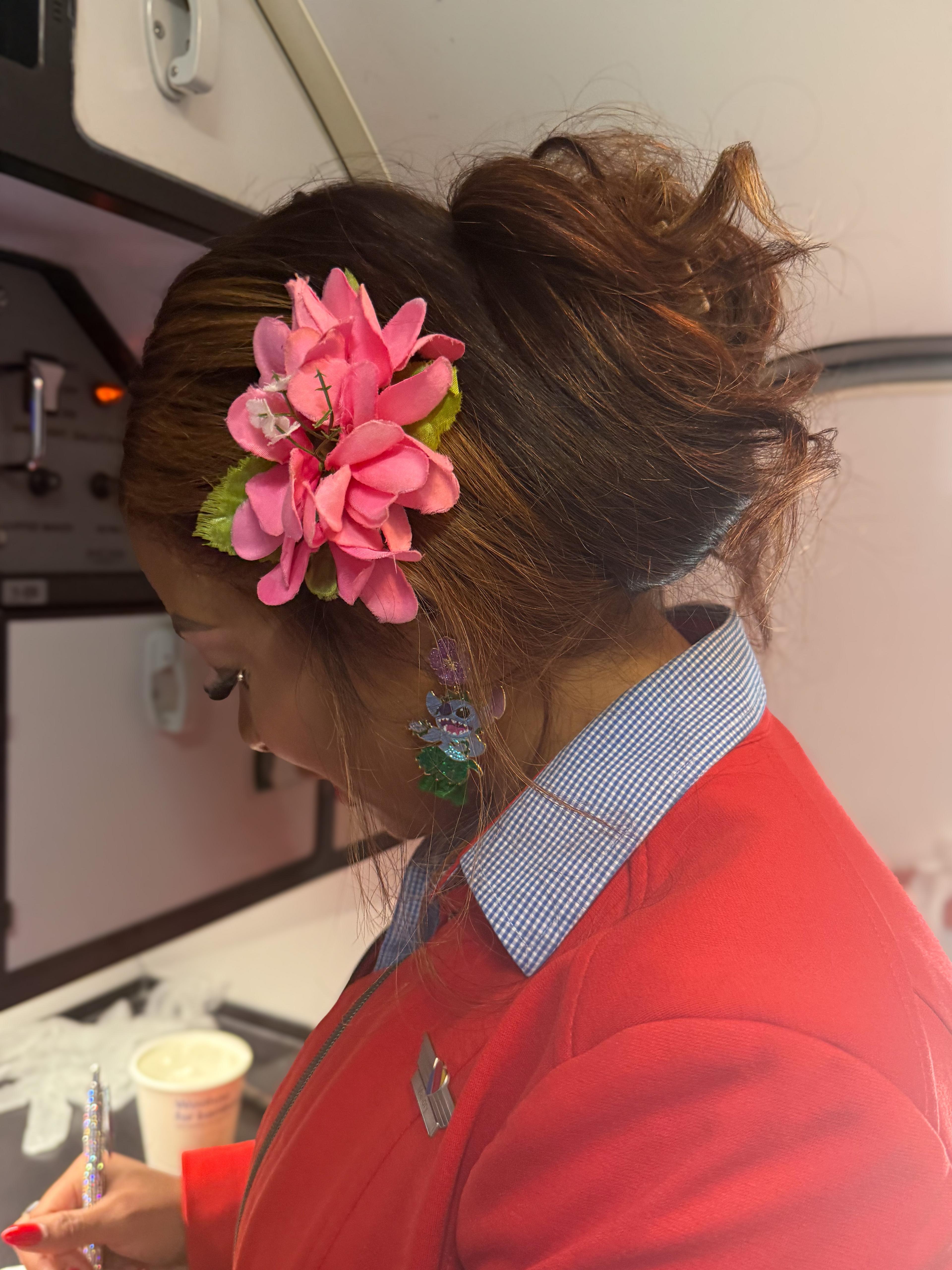 A flight attendant, adorned with a pink flower in her hair, writes inside an airplane galley.