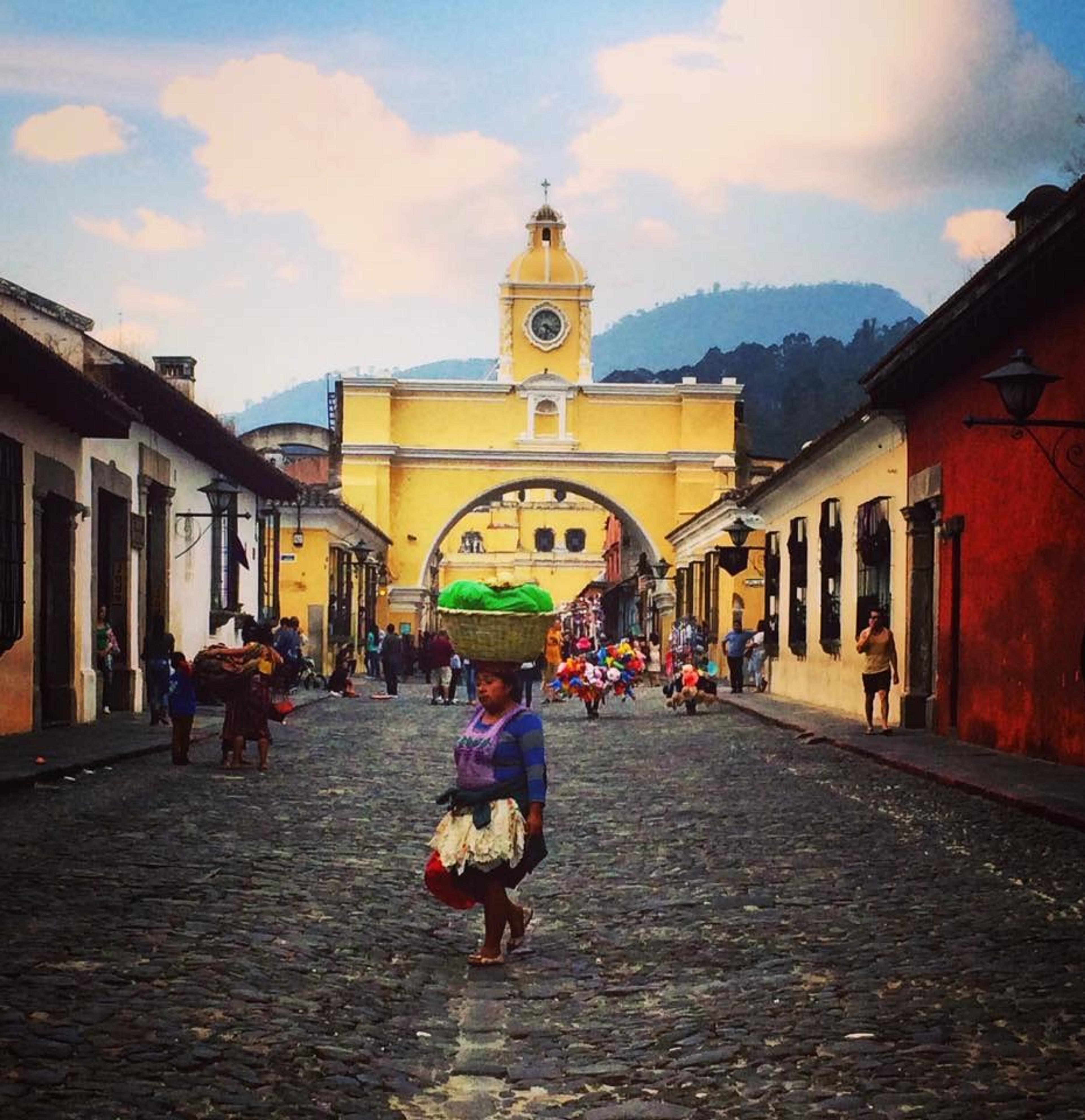 A woman balances a basket on her head while walking down the cobblestone street of Santa Catalina Arch in Antigua, Guatemala.