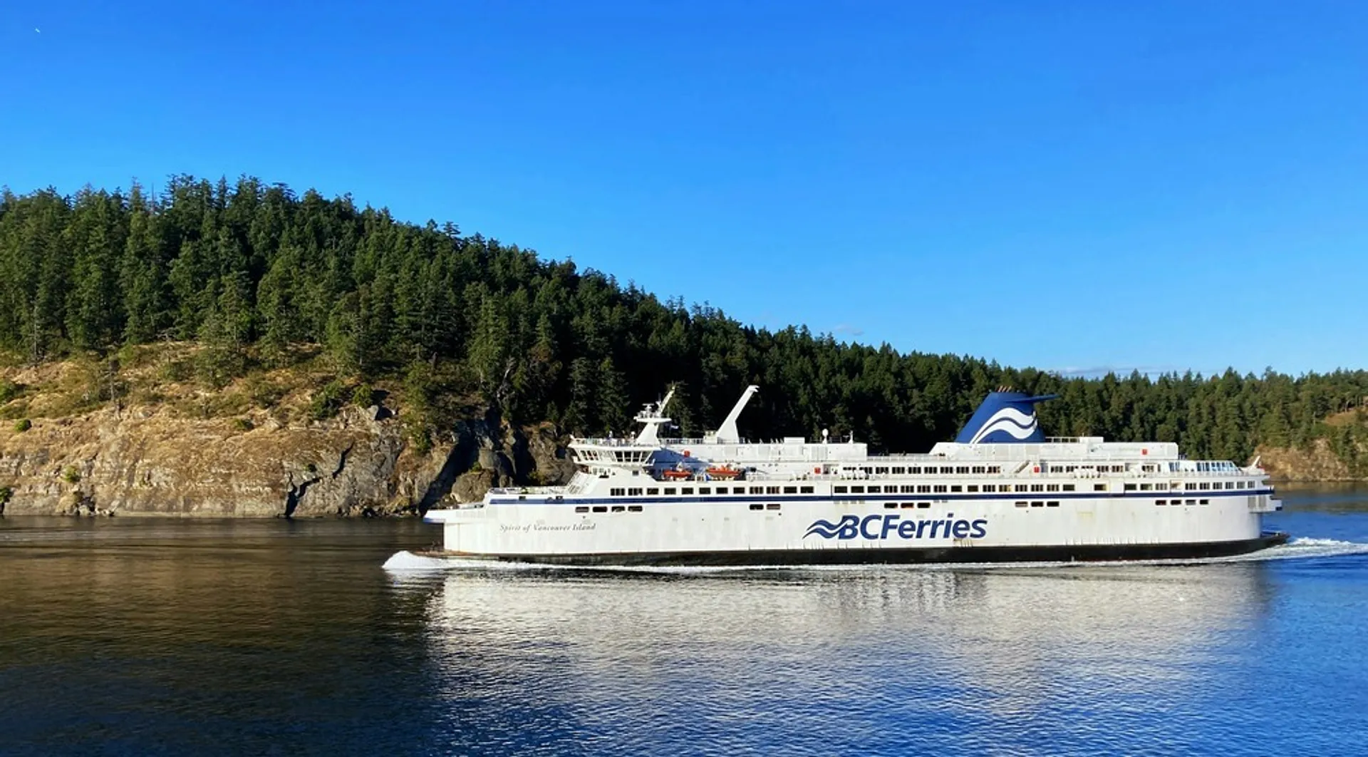 A BC Ferries vessel sails past a forested shoreline near Vancouver Island.