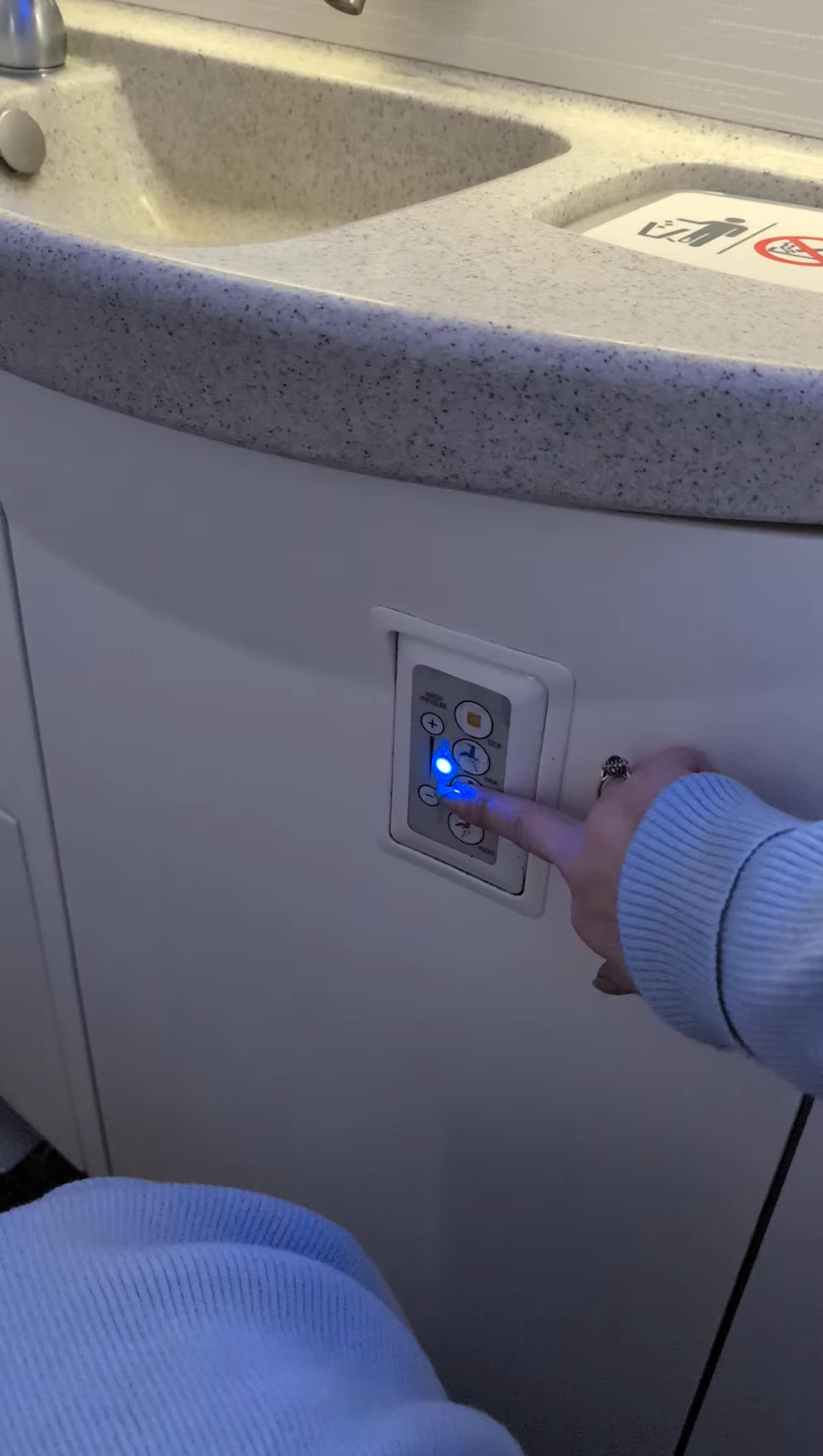 A person presses a button on a panel in an airplane lavatory.