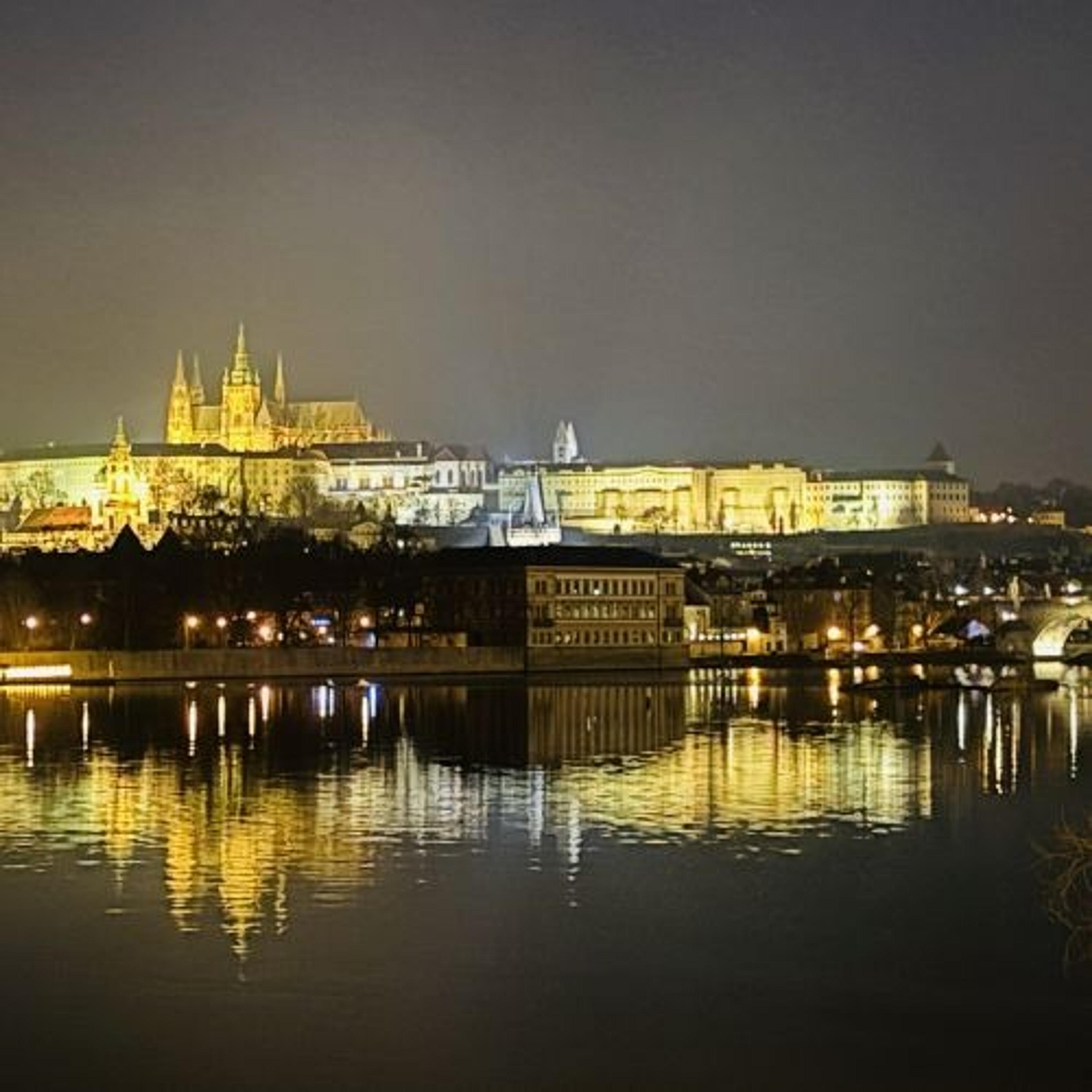 Prague Castle in the Czech Republic beautifully illuminated against the night sky, reflecting on the Vltava River.