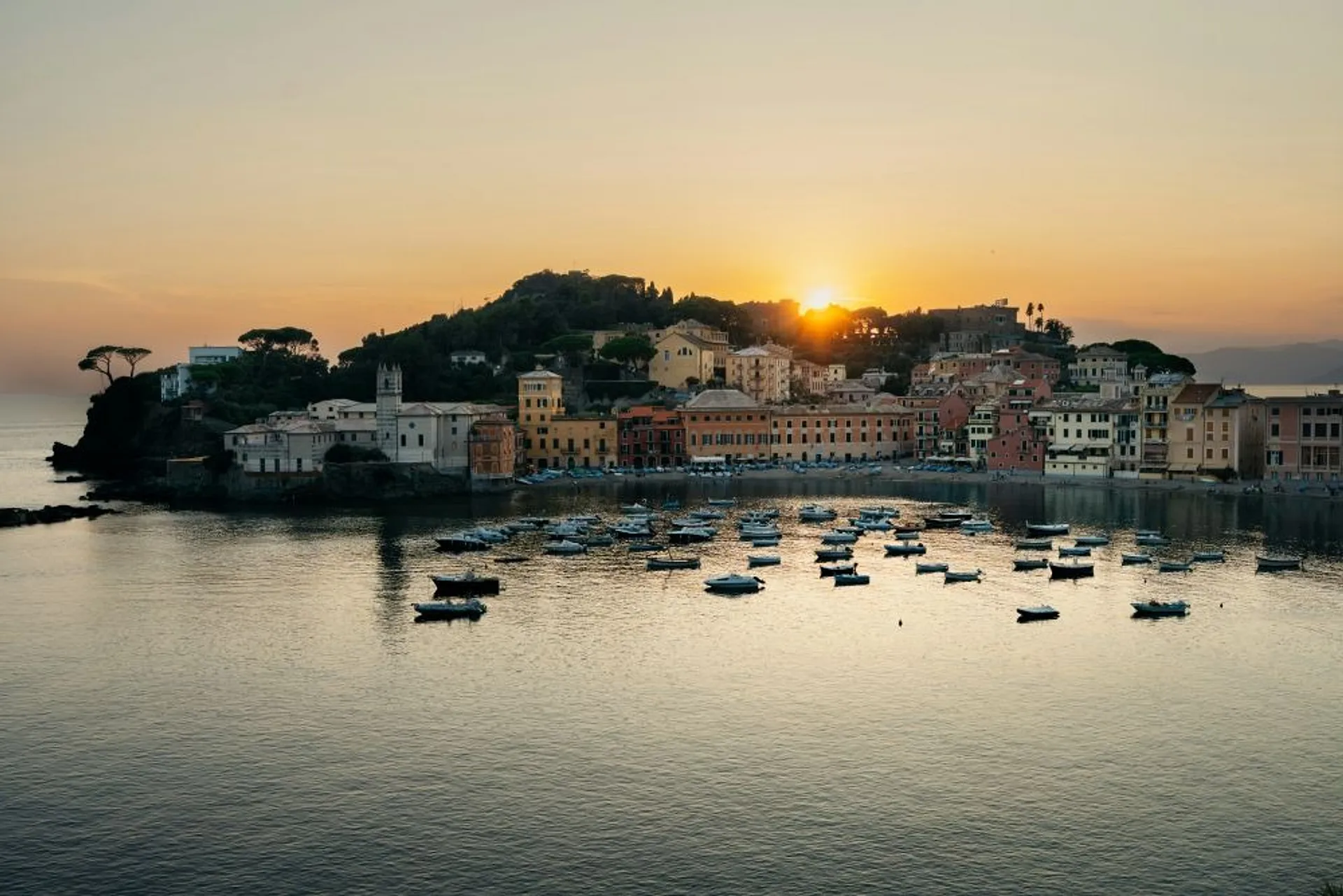 Sunset casts a warm glow over the charming coastal town of Sestri Levante in Italy, with its boats gently bobbing in the bay.