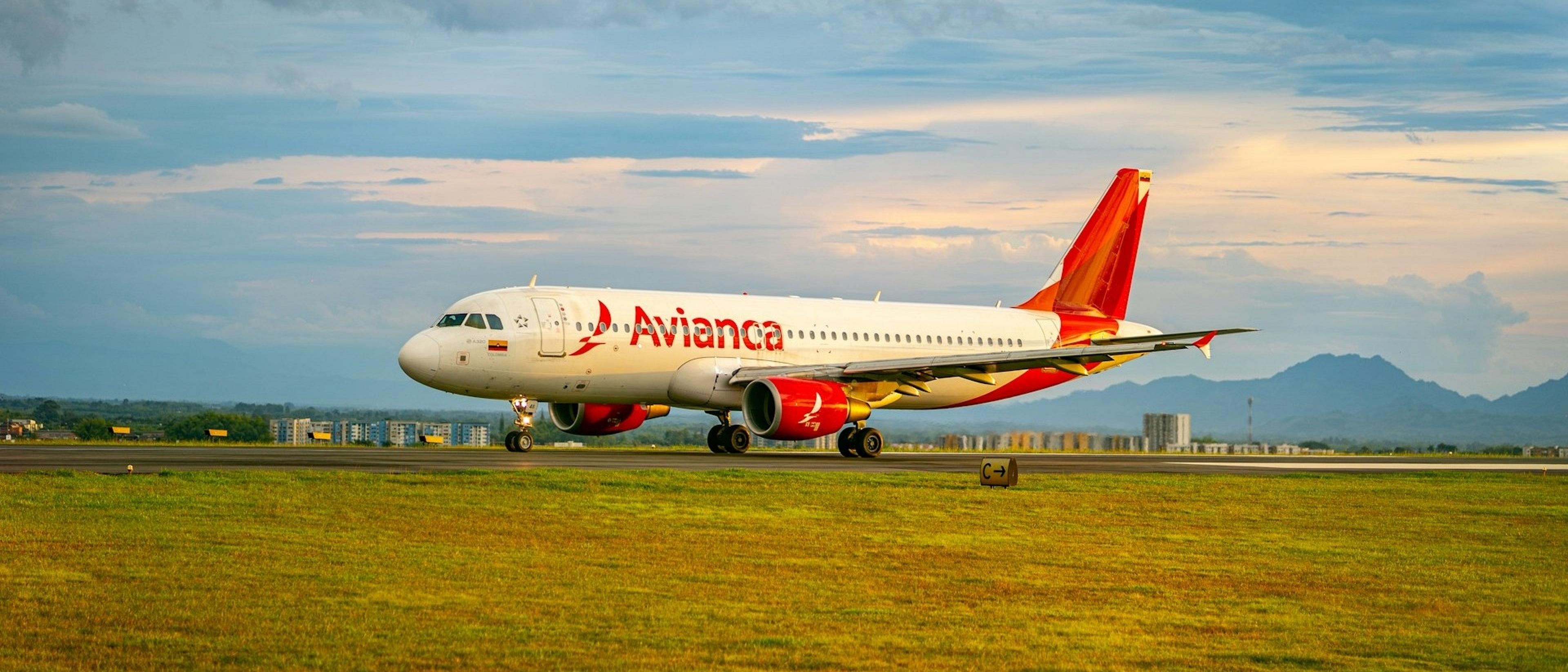 An Avianca plane taxis on the runway at Alfonso Bonilla Aragón International Airport, with mountains visible in the background.