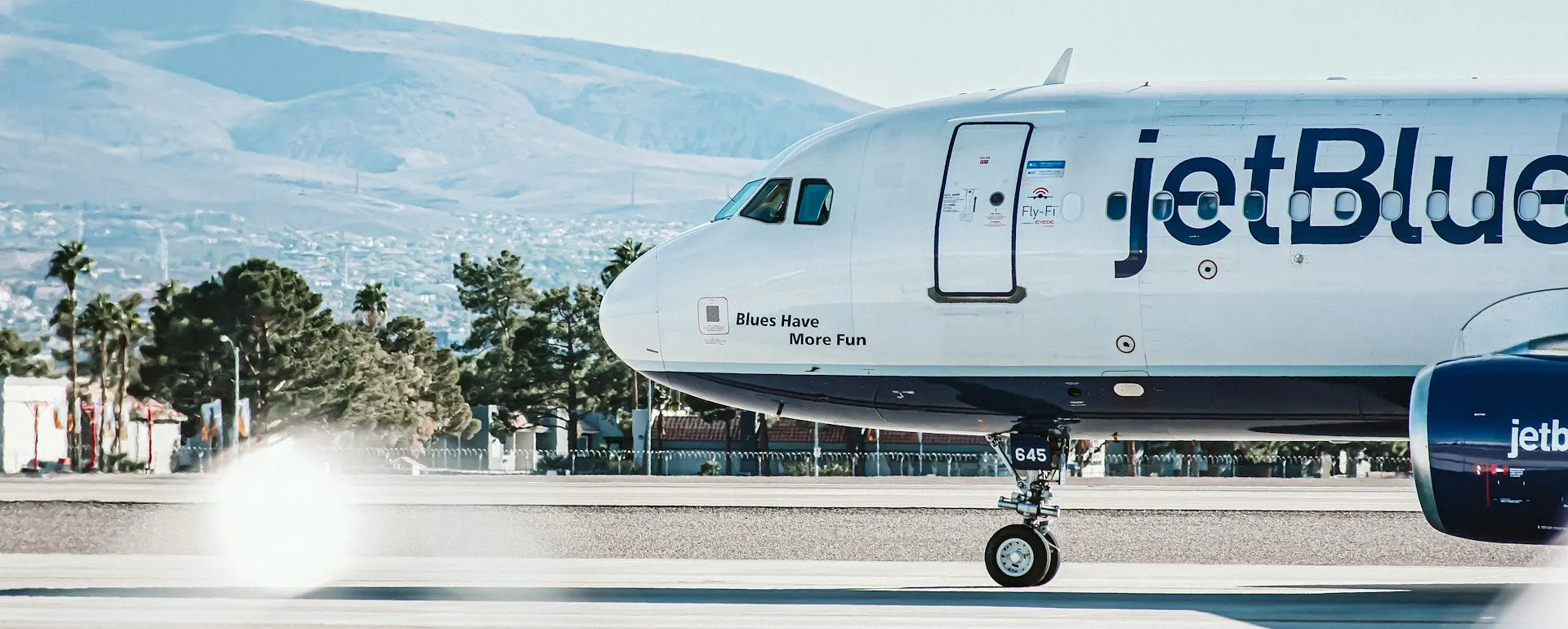 A JetBlue airplane taxis on a runway with the mountainous landscape of Las Vegas in the background.
