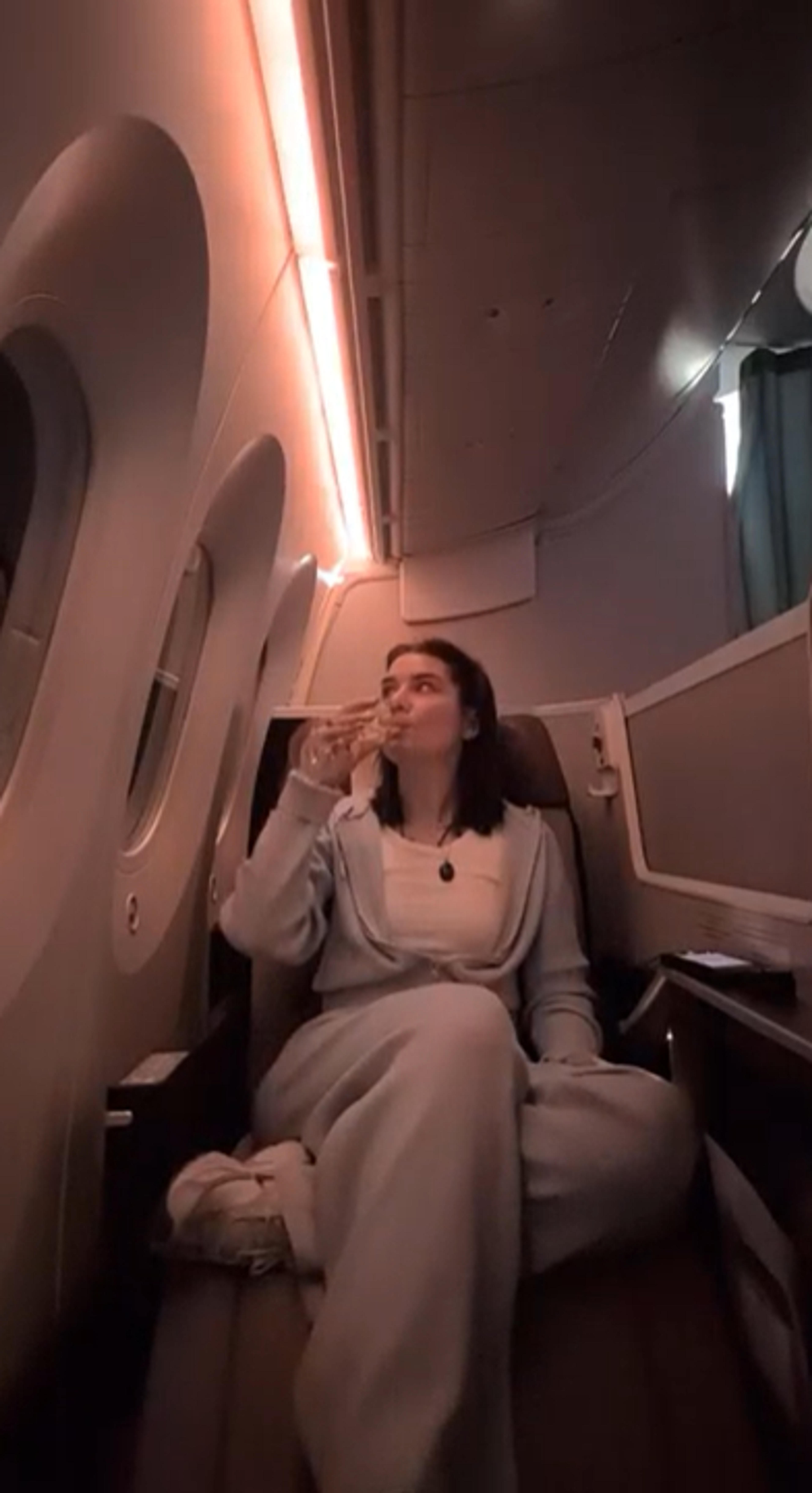 A passenger enjoys a drink in a dimly lit airplane cabin, likely traveling in a business class section.