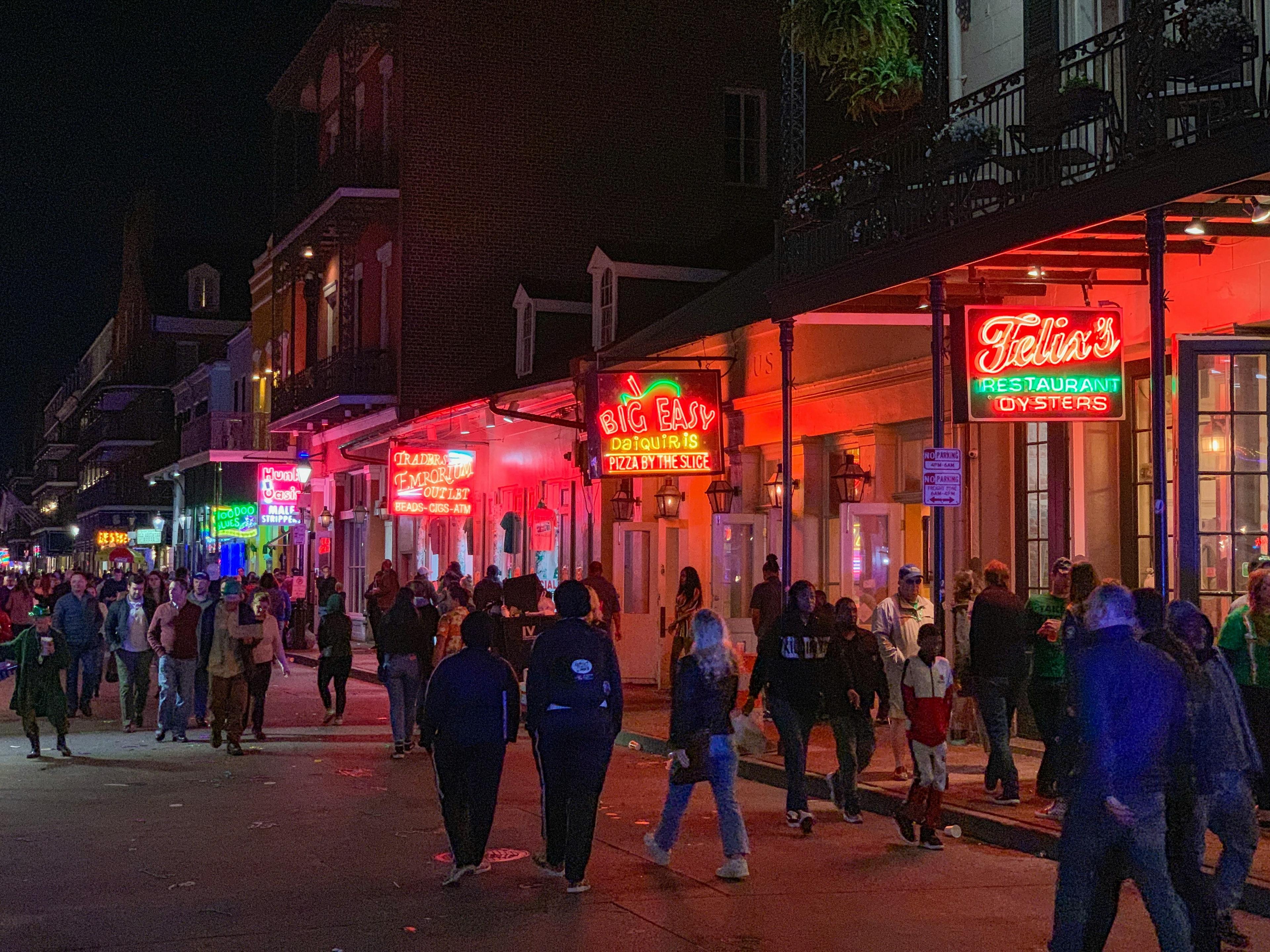 A lively night scene unfolds on Bourbon Street in New Orleans, featuring vibrant neon signs and a bustling crowd.