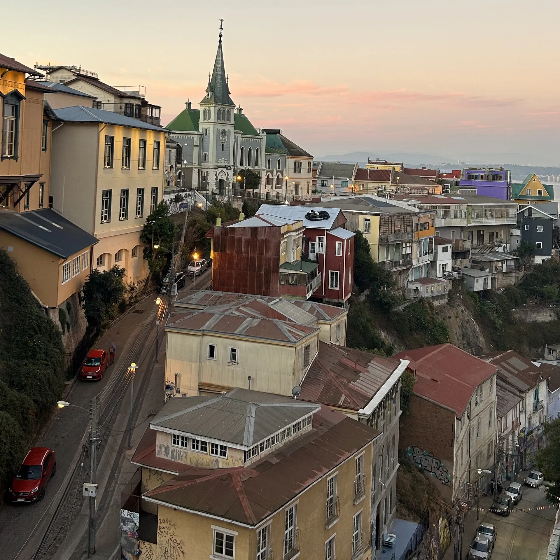 Colorful houses and a church spire characterize the hilly streets of Valparaíso, Chile at sunset.