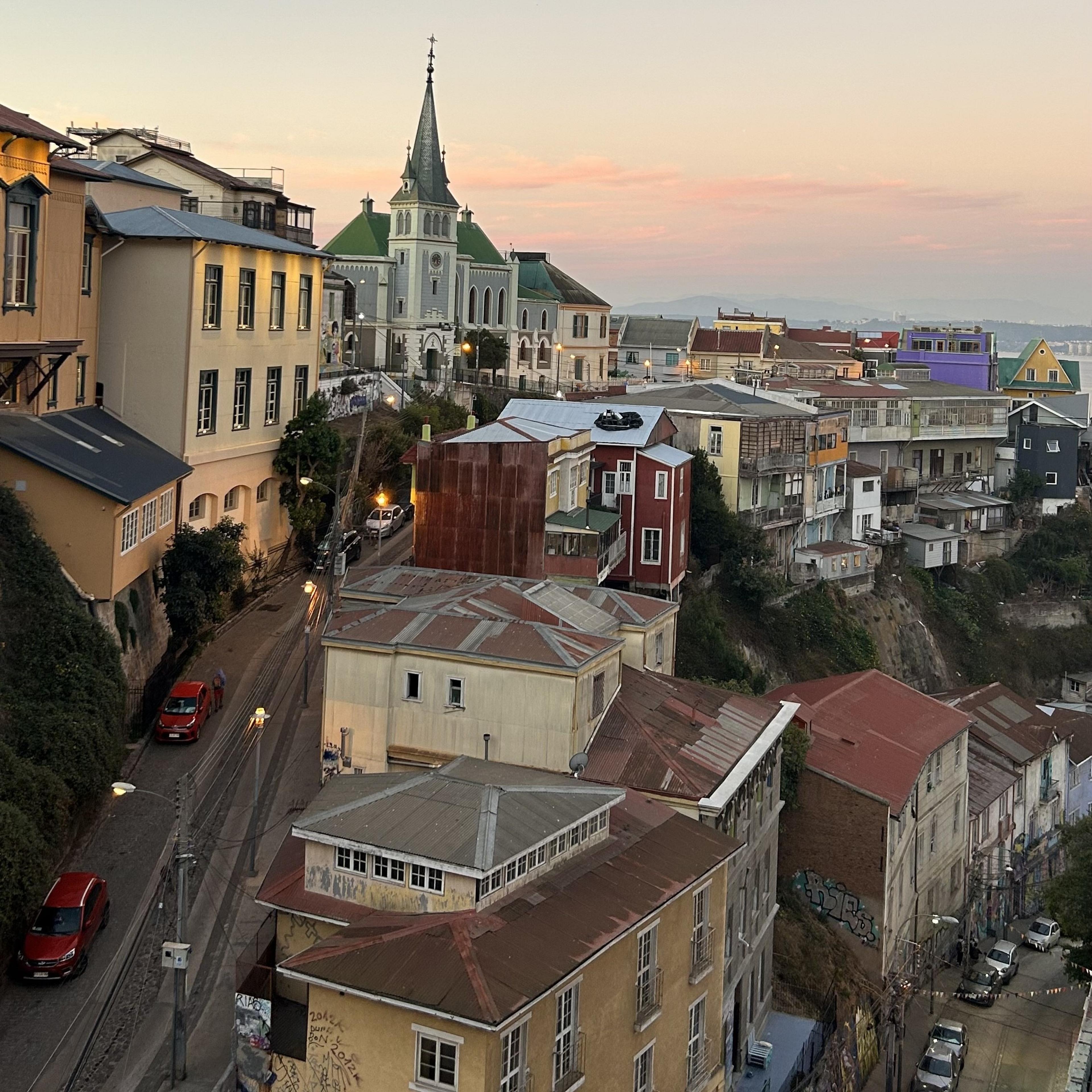 Colorful houses and a church spire characterize the hilly streets of Valparaíso, Chile at sunset.